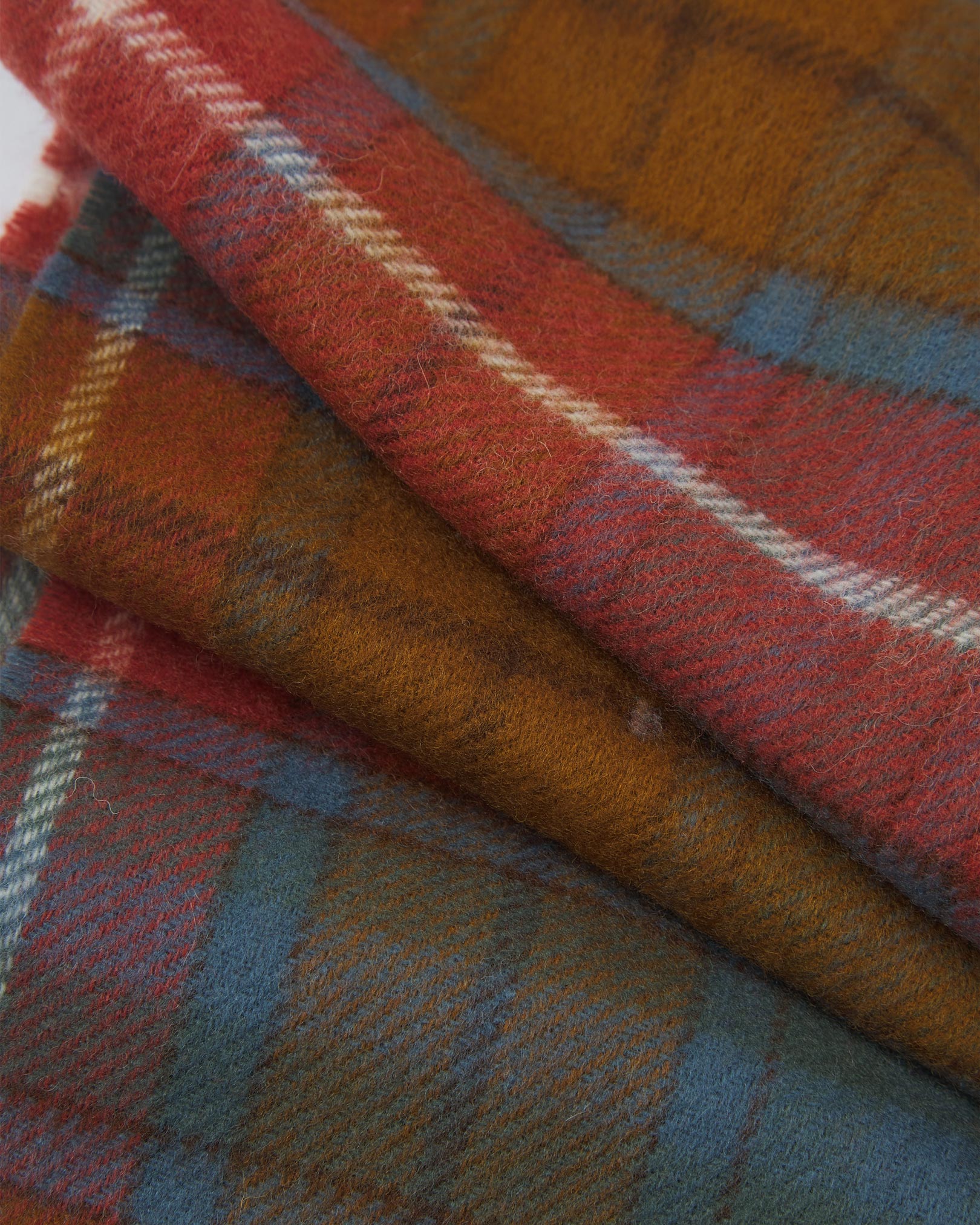 Ruffled close-up view of the UK-made, pure Merino wool 'Highlands tartan Antique Buchanan' scarf, presenting a closer view of the tan, rust-red, and blue interlocking tartan pattern.