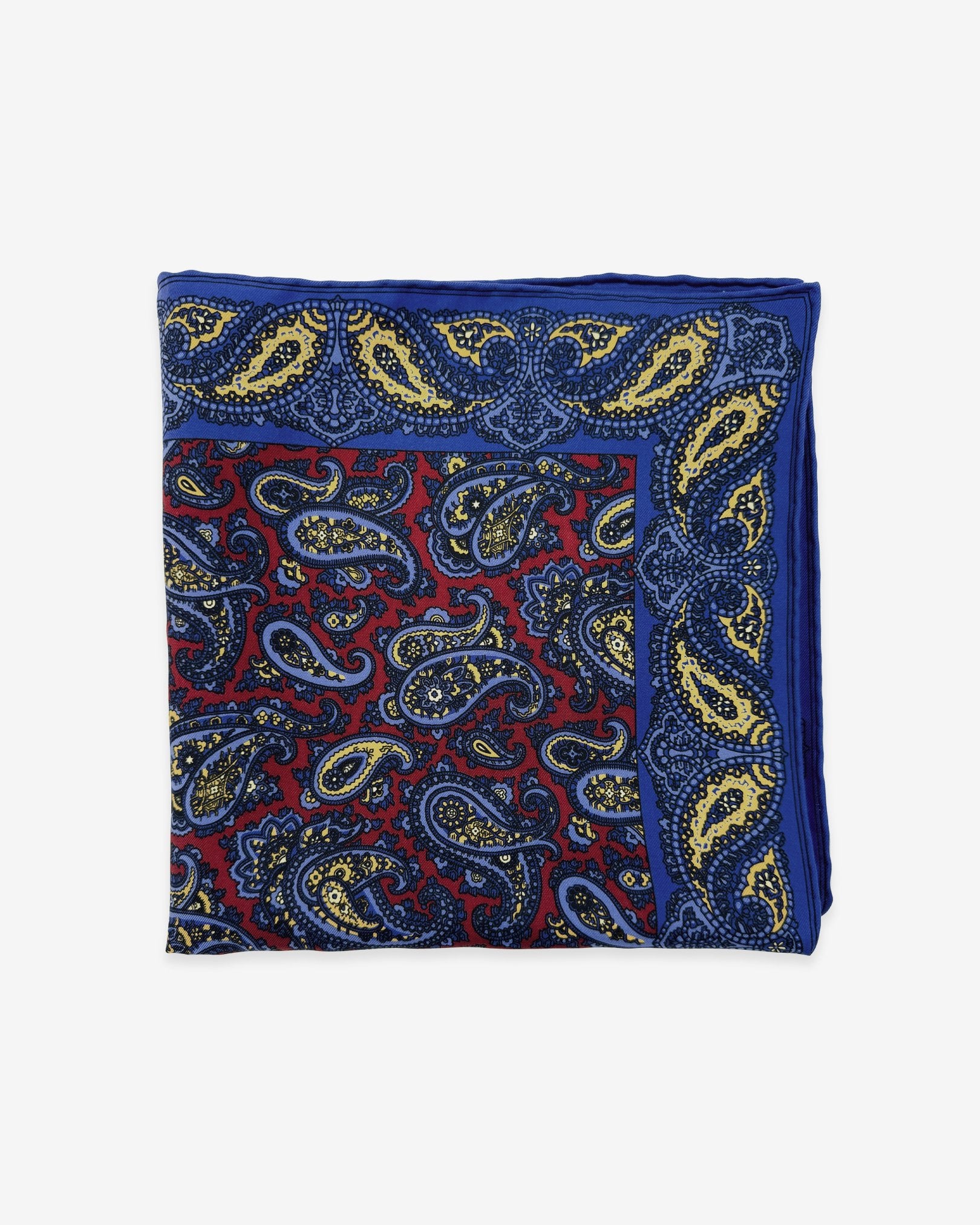 The 'Avebury' pocket square from SOHO Scarves Madder silk collection. Folded into a quarter, showing the blue, red and yellow paisley design against a deep red background.