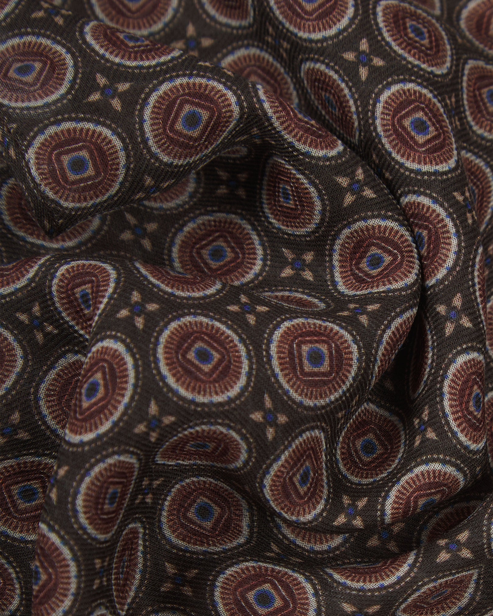 A ruffled close-up of the Bellingham 'Mahogany Daze' bohemian wide scarf, showing the soft modal and wool blend fabric with intricate concentric circular motifs in cream, maroon and subtle purple on a rich brown background.