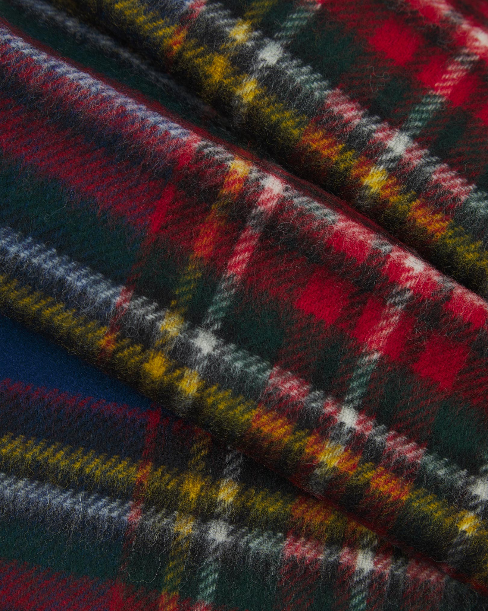 Ruffled close-up view of the UK-made, pure Merino wool 'Highlands' tartan in blue scarf, presenting a closer view of the red, yellow, white, and green interlocking tartan pattern.