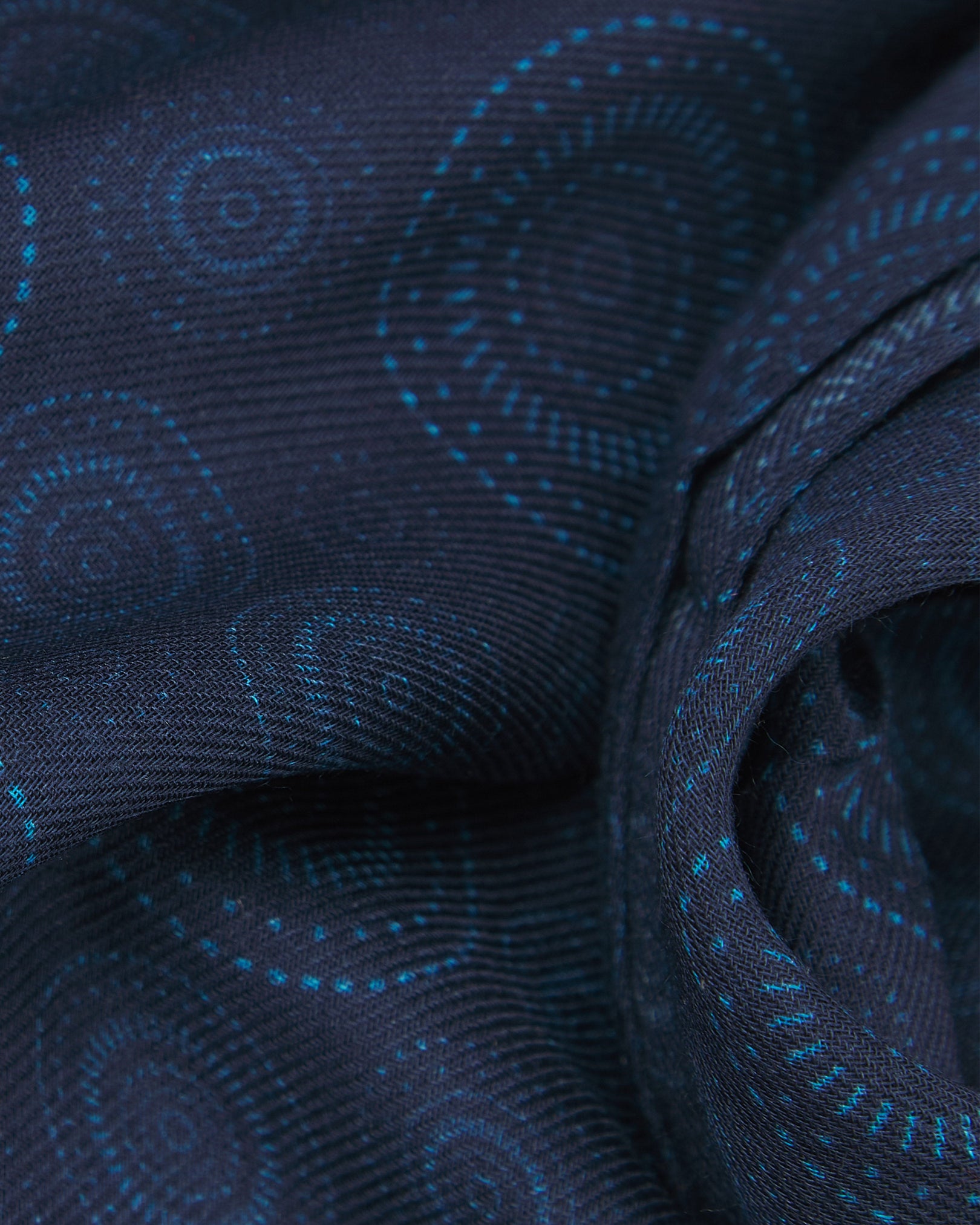 A ruffled close-up of the 'Circles' blue bohemian wide scarf, showing the soft modal and wool blend fabric with concentric Op art-inspired disc motifs in light blue on a dark blue background.