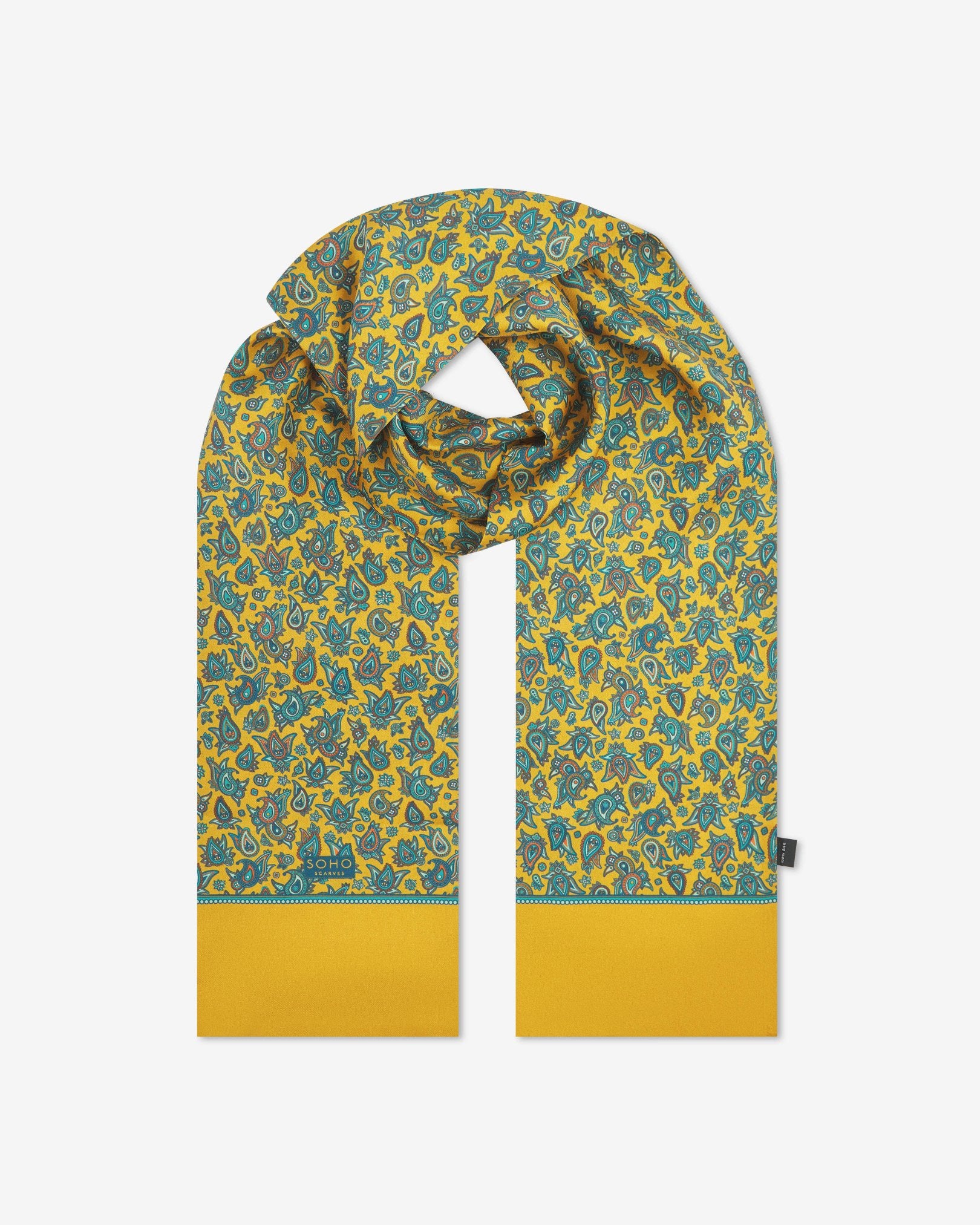 The 'Buttermere' gold silk scarf looped with both ends parallel to effectively display the full repeat pattern of blue, blue-green, orange, and yellow paisley patterns on an gold background.