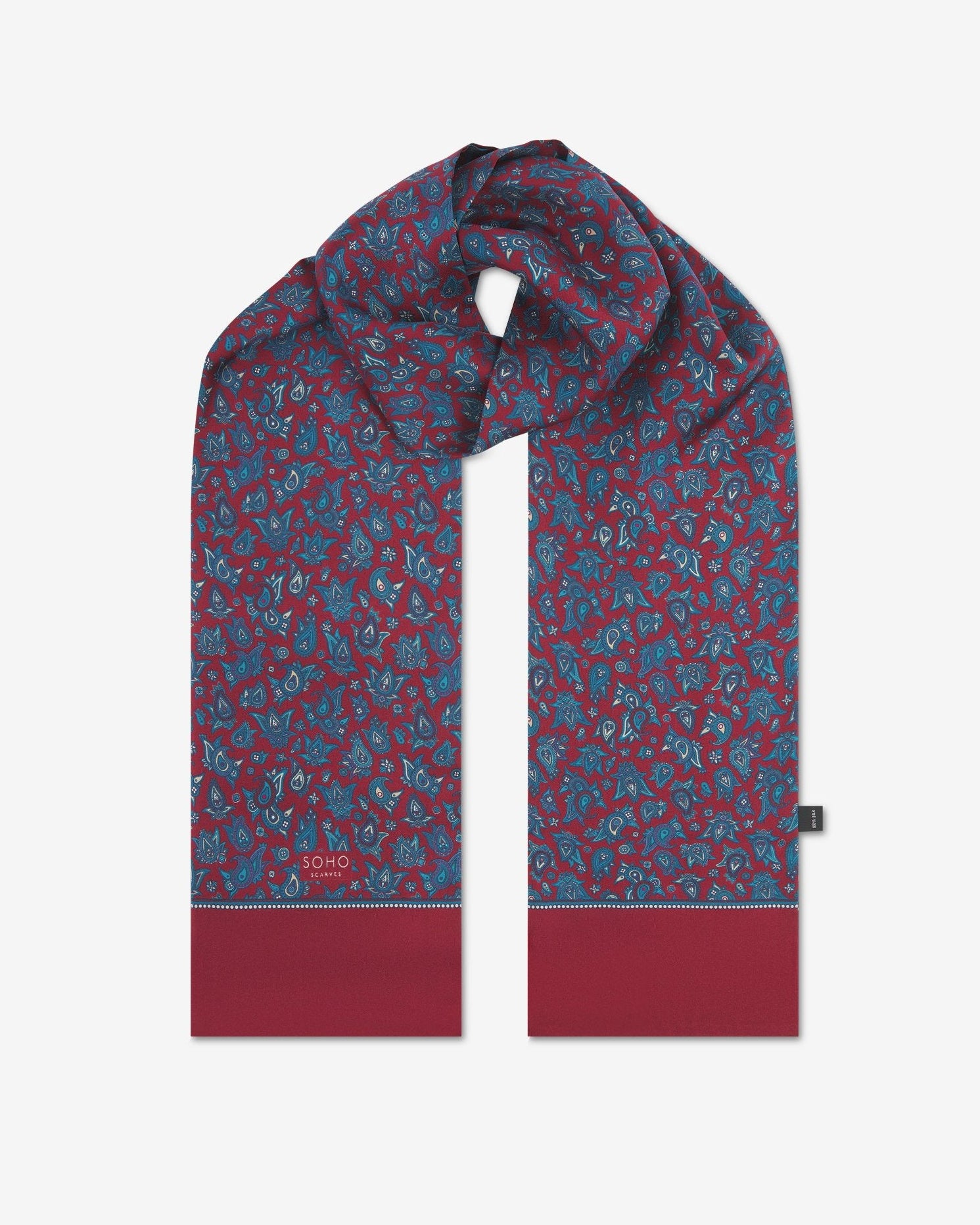 The 'Buttermere' rust silk scarf looped with both ends parallel to effectively display the full repeat pattern of blue and blue-green paisley patterns on an rust background