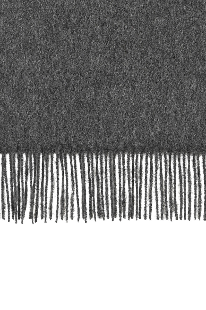 Perfectly horizontal view of the fringe of a charcoal pure cashmere scarf from Soho Scarves against a white background.