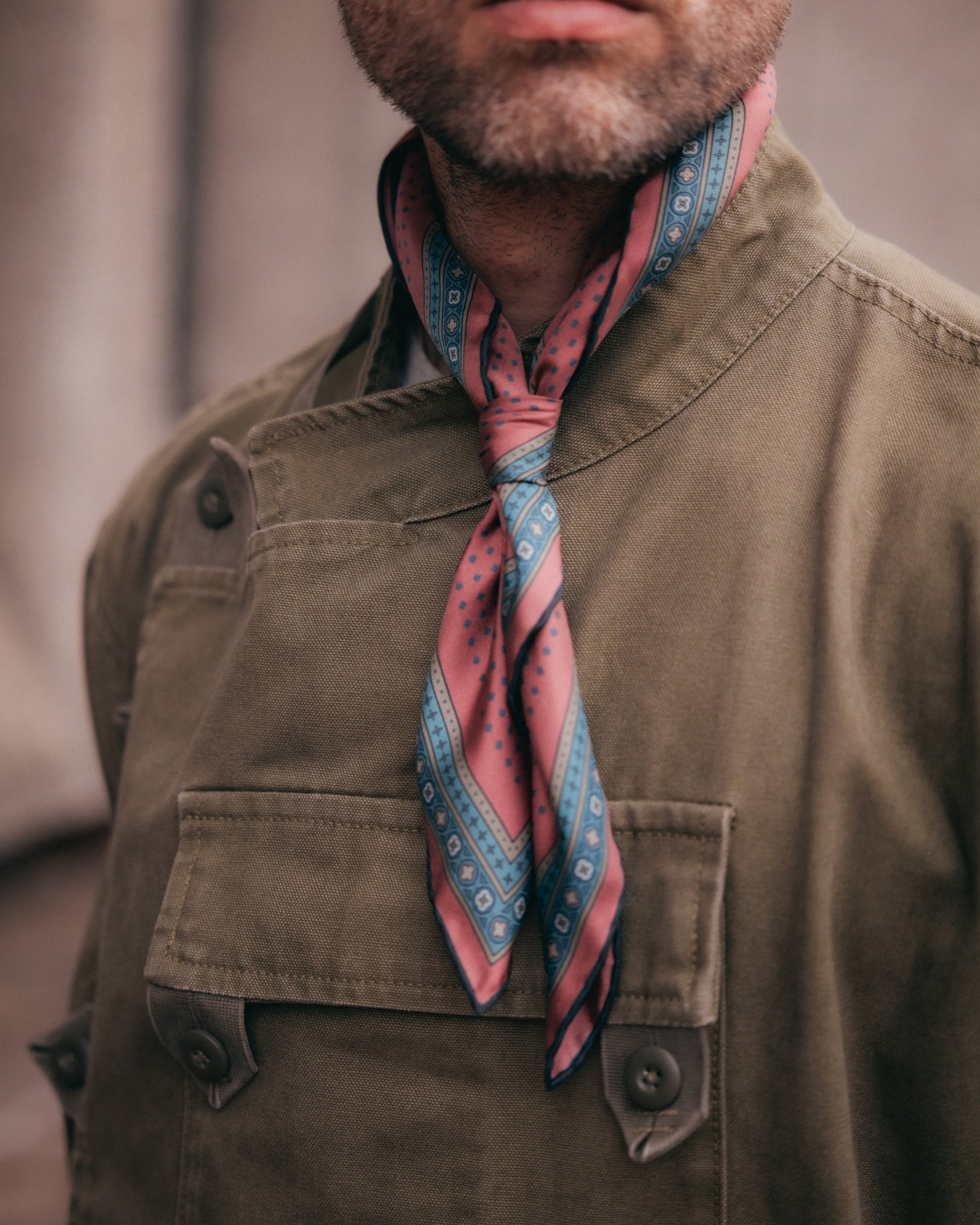 A close-up of a man wearing a brown utility jacket and the Chiswick 'Berry' patterned silk neckerchief from SOHO Scarves.