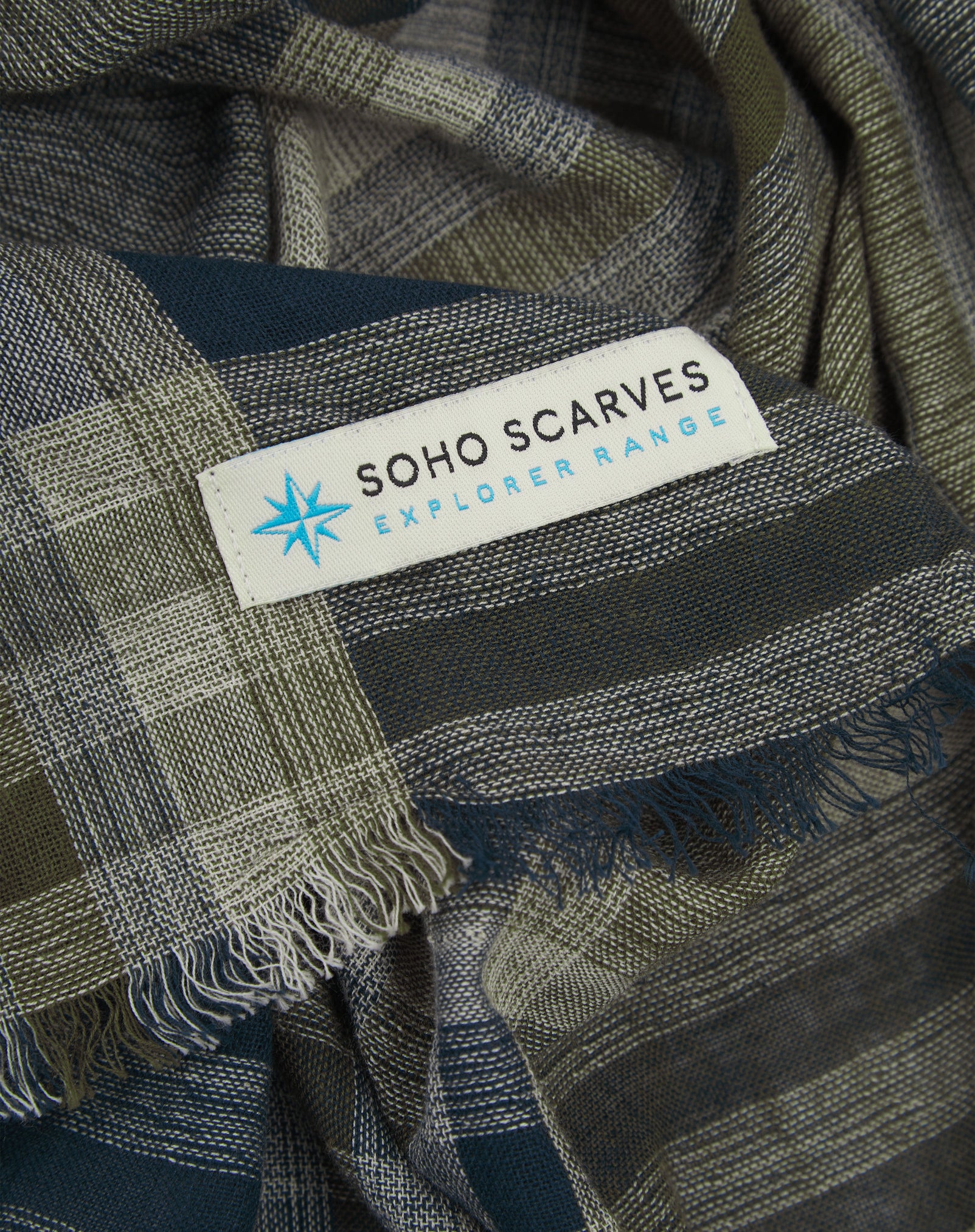 Ruffled close-up view of the pure cotton 'Norgay' scarf, presenting a closer view of the navy, olive, and grey yarns which make up the Tartan pattern.