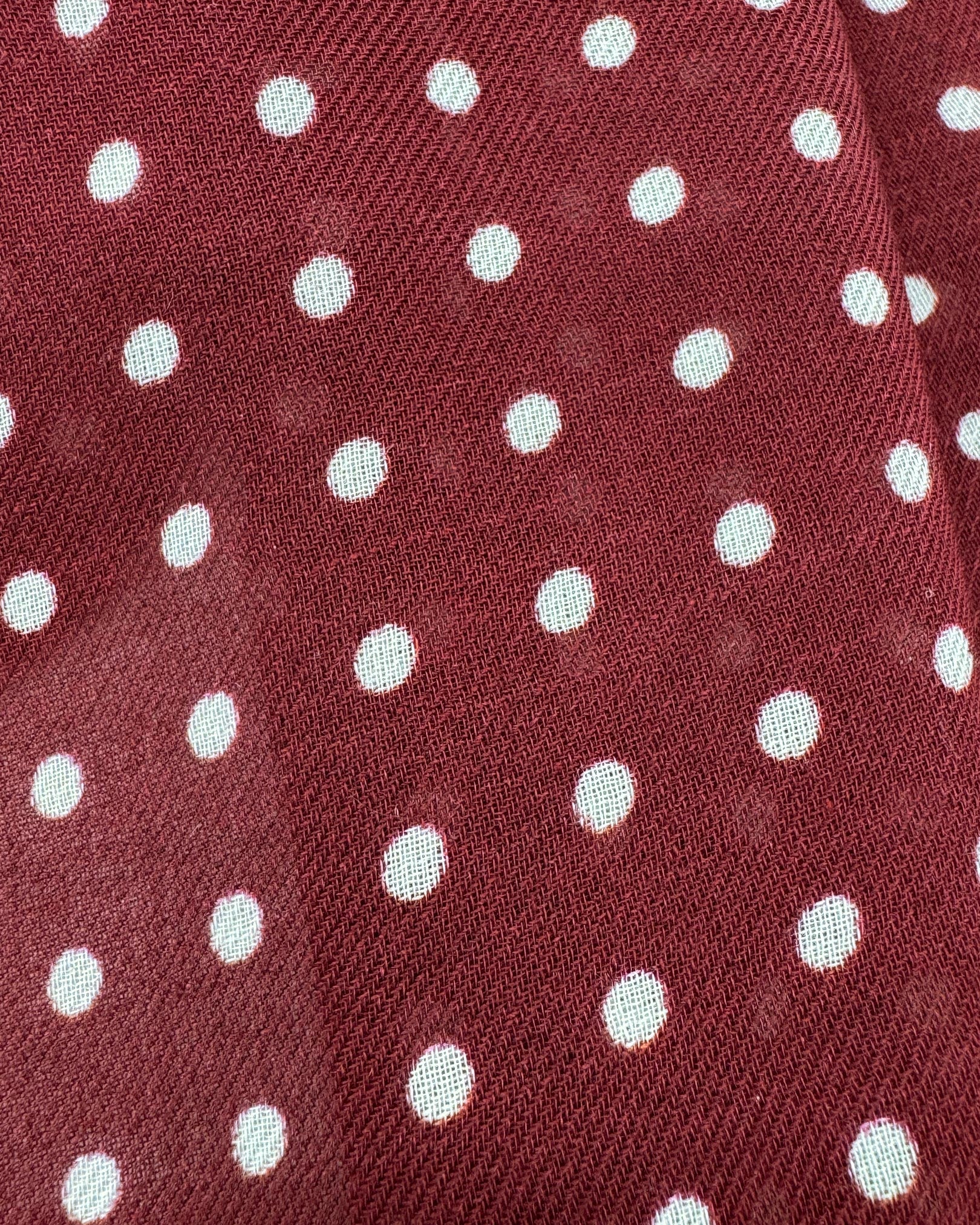 A flat, close up view of 'The Sapporo' wide scarf. Clearly showing the modal and wool fabric and attractive white polka dot pattern against a burgundy background.