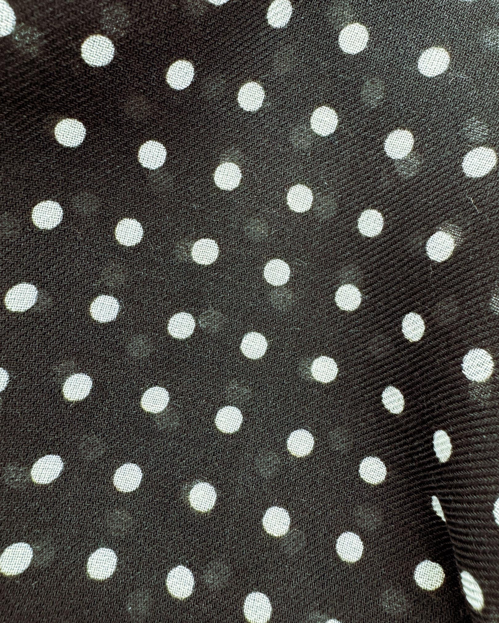 A flat, close up view of 'The Shinagwa' wide scarf. Clearly showing the modal and wool fabric and attractive white polka dot pattern against a black background.