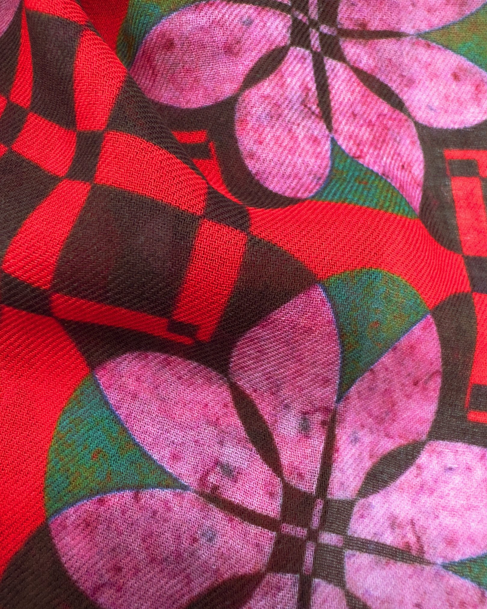 A flat, close-up view of the 'Trio 2' wide scarf. Clearly showing the modal and wool fabric and attractive pink floral pattern complemented by green, red and black geometric patterns.