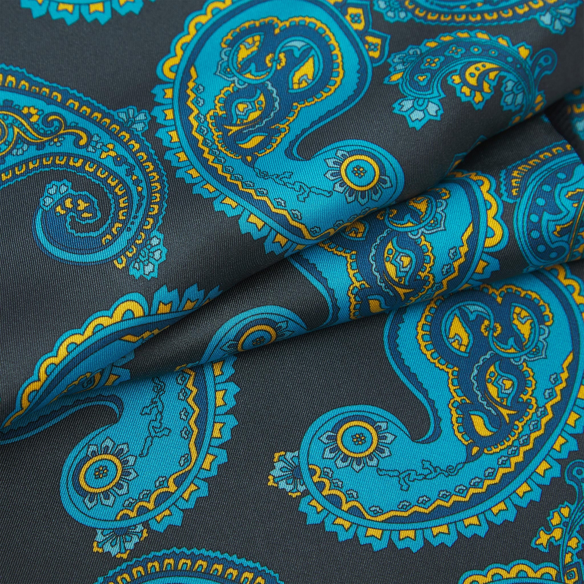 Ruffled close-up view of the Bridle silk scarf, presenting a closer view of the cyan paisley patterns with blue and gold accents against a dark grey background.