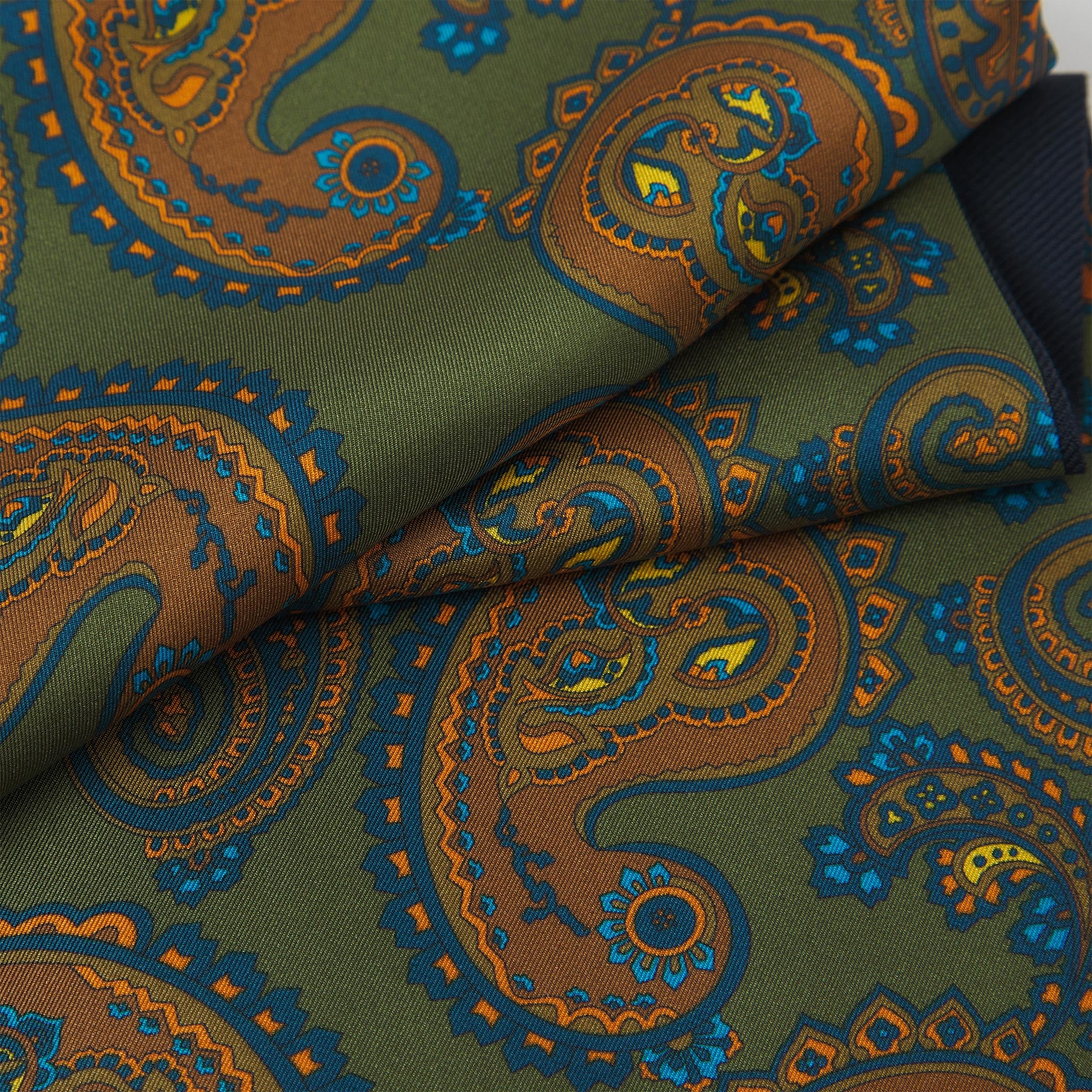 Ruffled close-up view of the Carlisle silk scarf, presenting a closer view of the orange paisley patterns enhanced with blue and gold accents against a rich green background