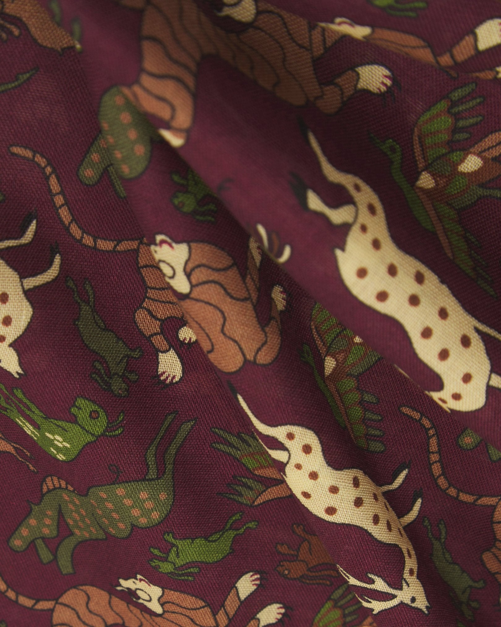 A ruffled, close-up view of the UK-made burgundy silk-wool scarf with stylised woodland creatures. Clearly showing the premium silk and wool weave and the detailed multicoloured animal patterns against a rich burgundy background.