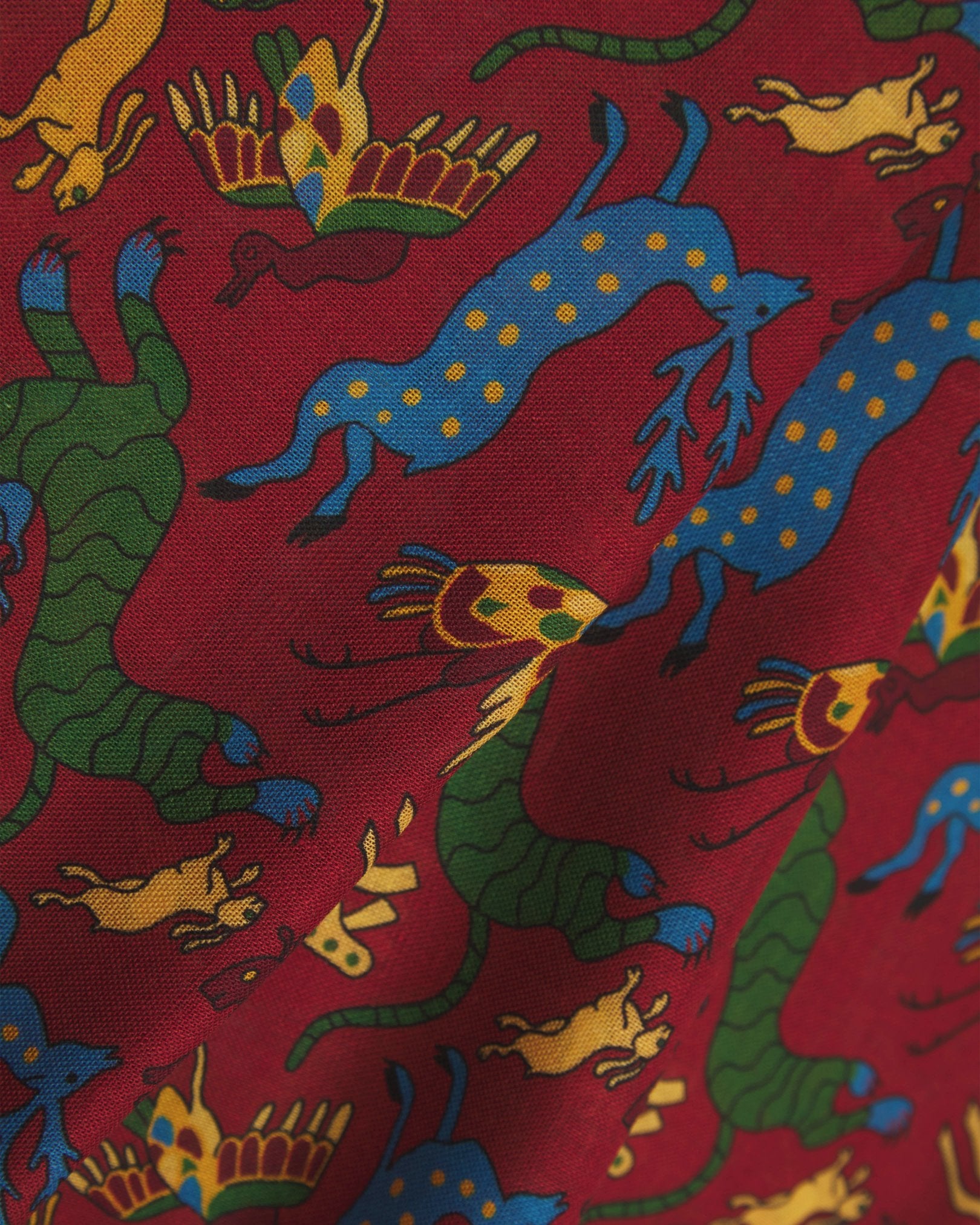 A flat, close-up view of the UK-made ‘rust-red’ silk-wool scarf with stylised woodland creatures. Clearly showing the premium silk and wool weave and the detailed multicoloured animal and floral patterns against a warm red background.