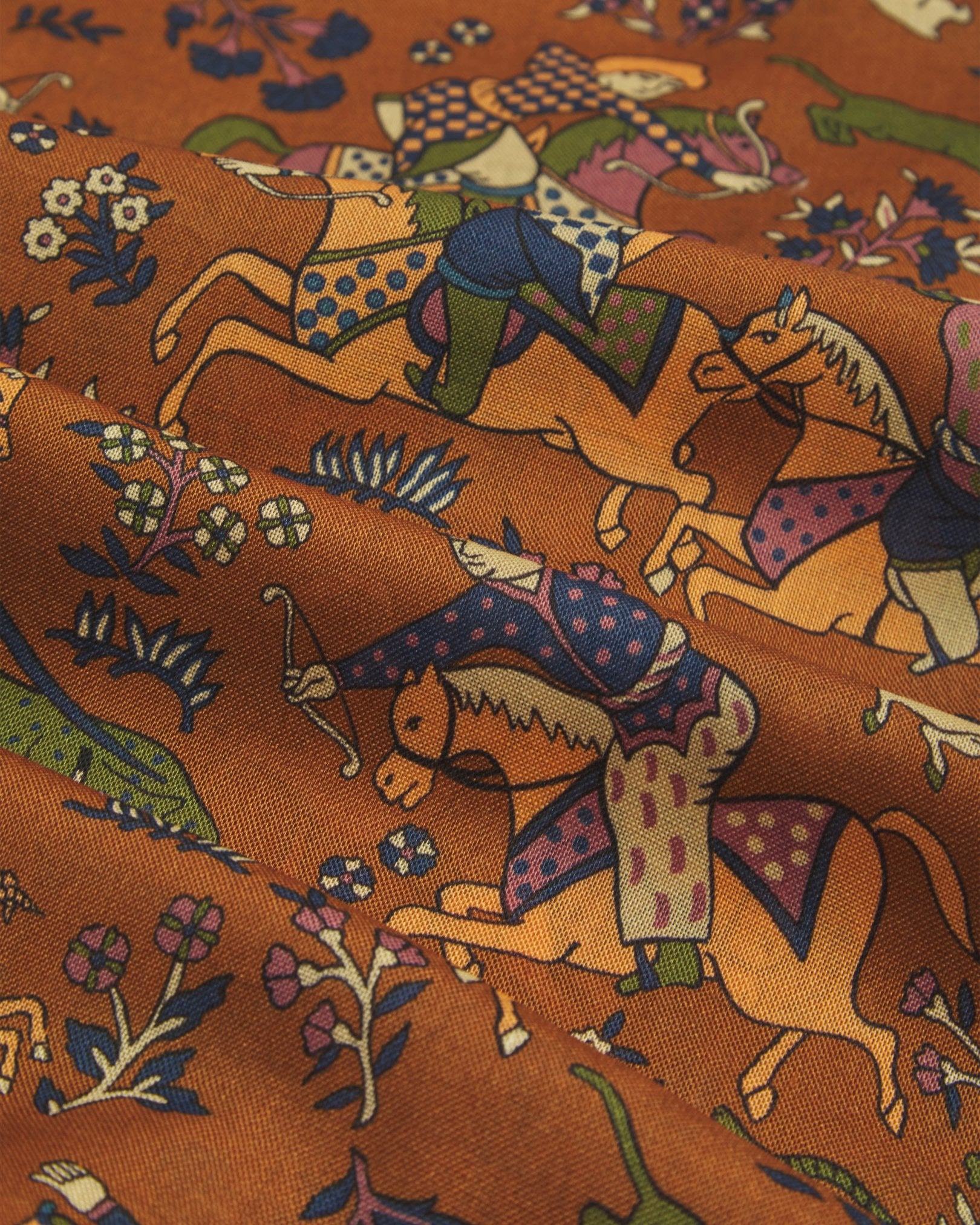 A flat, close-up view of the UK-made ‘dull gold’ silk-wool scarf with ancient hunting scenes from the far-east. Clearly showing the premium silk and wool weave and the detailed multicoloured animal and floral patterns against a dull gold background.