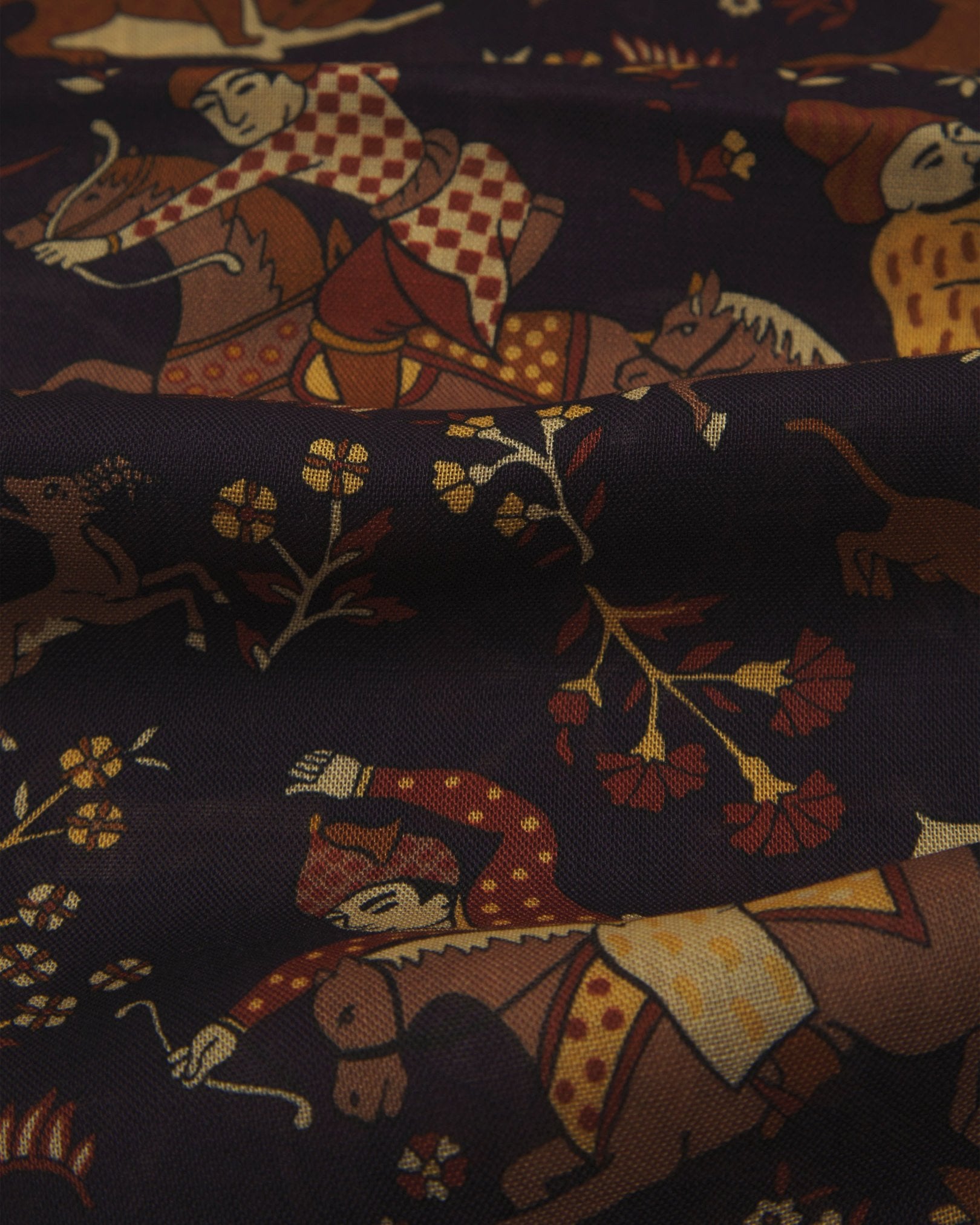 A ruffled, close-up view of the UK-made indigo-blue silk and wool scarf depicting ancient far-eastern hunting scenes. Clearly showing the premium silk and wool weave and the detailed multicoloured animal and floral patterns against an indigo background.