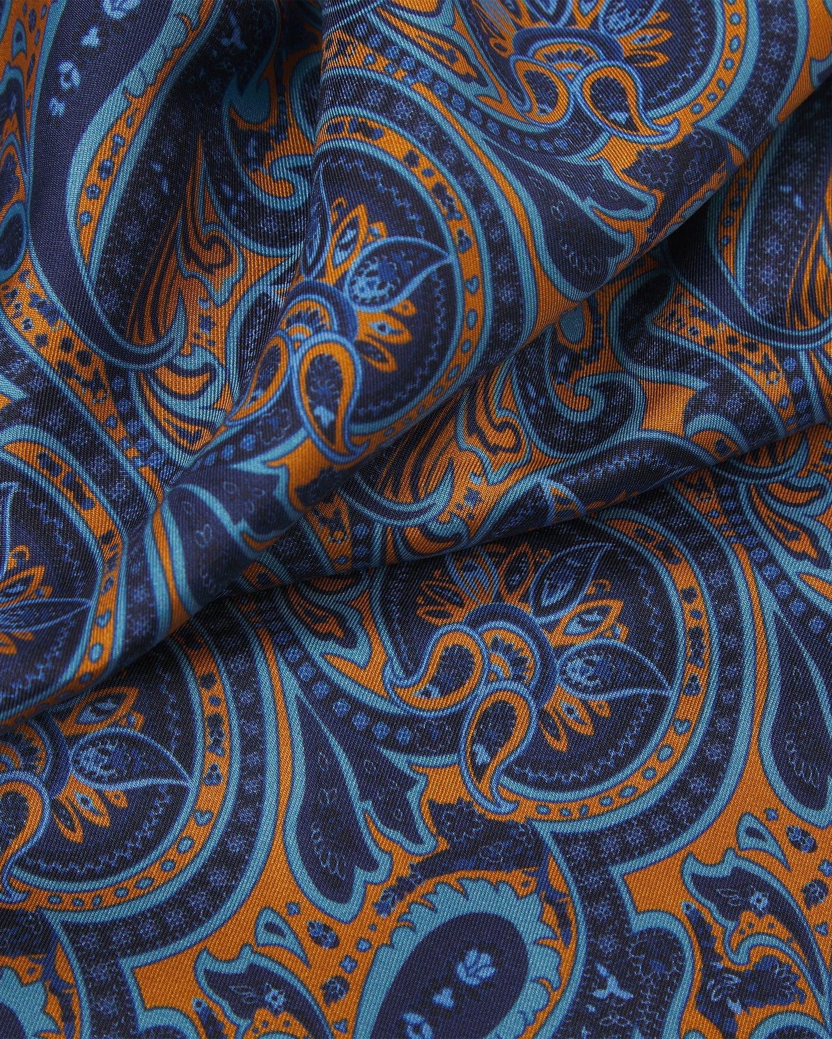 Ruffled close-up view of the Roppongi silk scarf, presenting a closer view of the navy-blue coloured fabric with light blue and orange patterns.