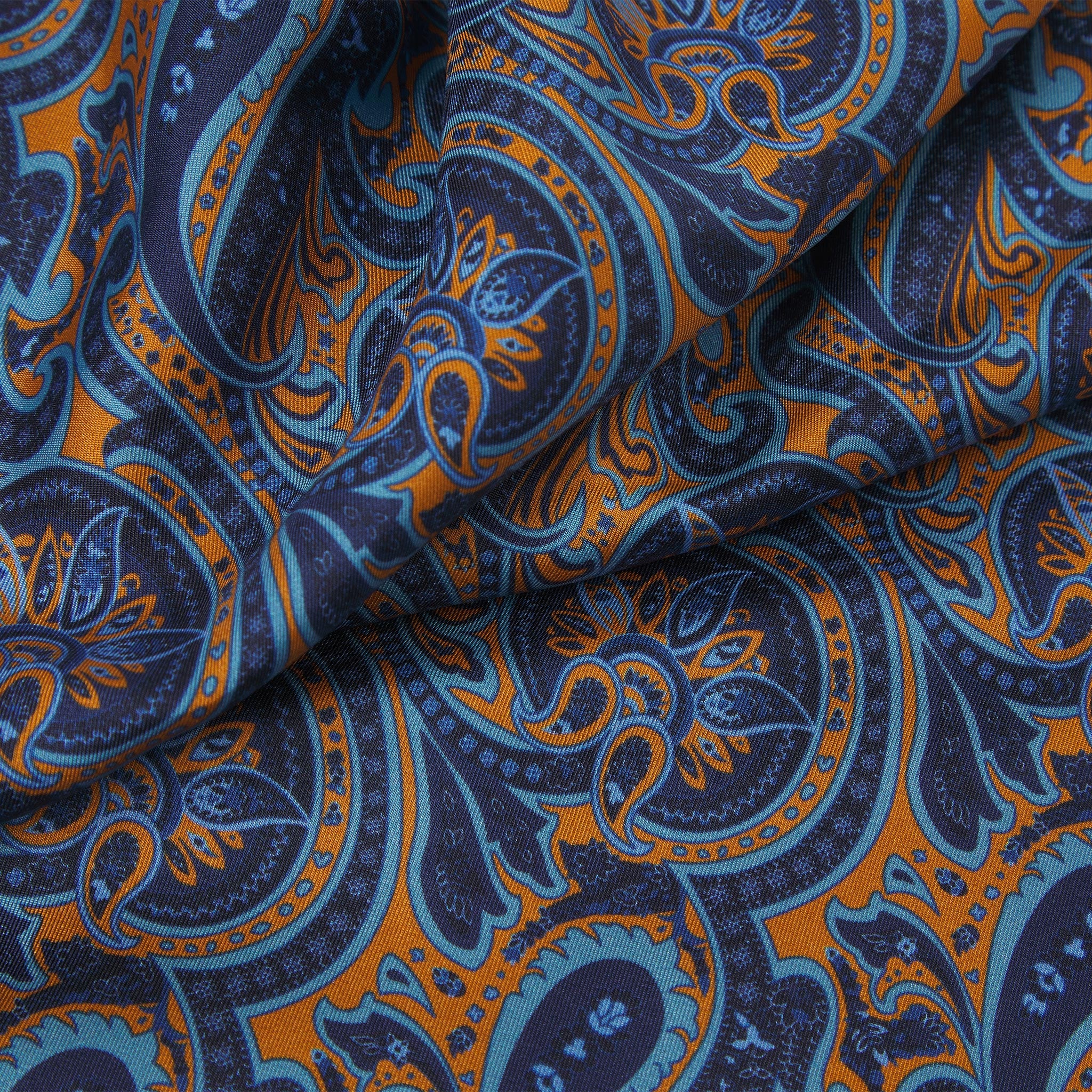 Ruffled close-up view of the Roppongi silk scarf, presenting a closer view of the navy-blue coloured fabric with light blue and orange patterns.