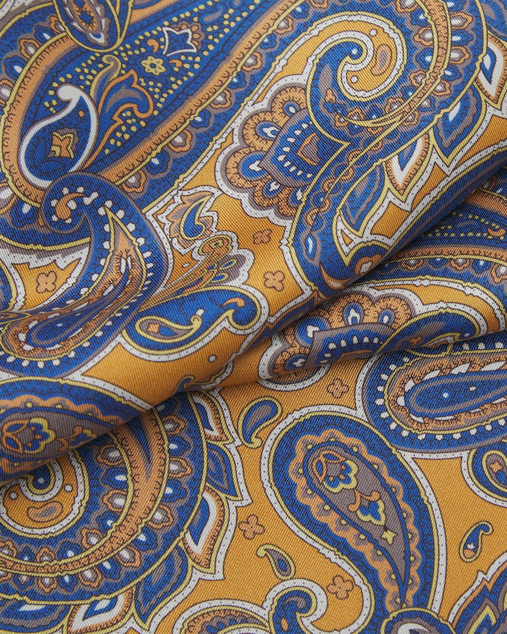 Ruffled close-up view of the Vandam silk scarf, presenting a closer view of the warm, golden background and blue paisley patterns.