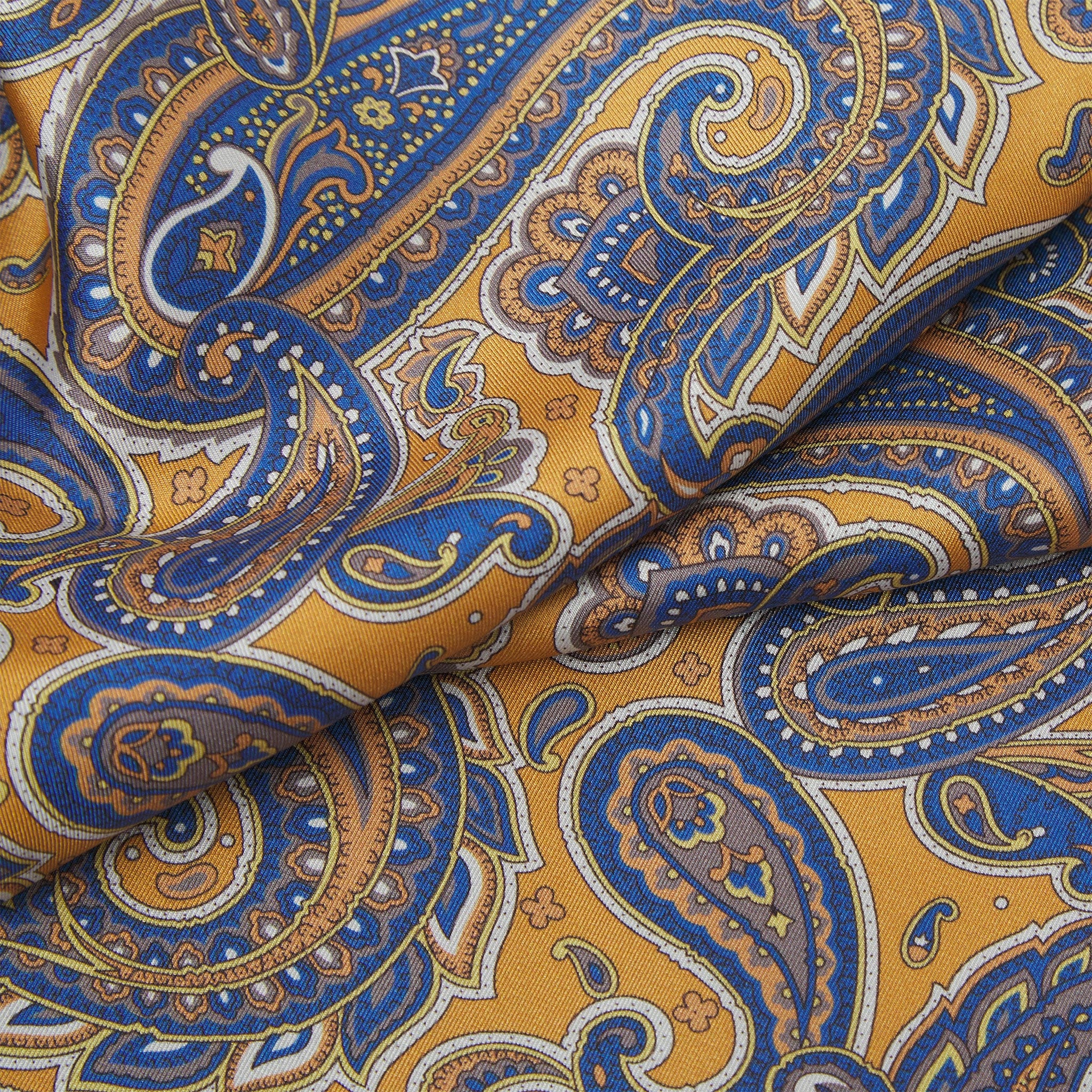 Ruffled close-up view of the Vandam silk scarf, presenting a closer view of the warm, golden background and blue paisley patterns.