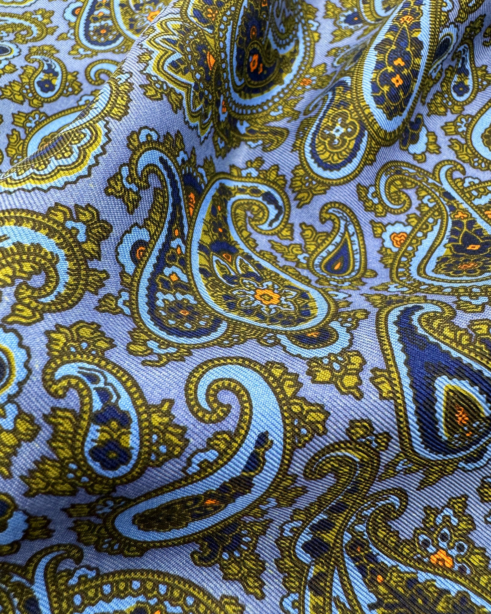 A ruffled close-up of the 'Acton' pocket square, presenting a closer view of the lime green and blue paisley patterns against the attractive lustre of the madder silk material. 
