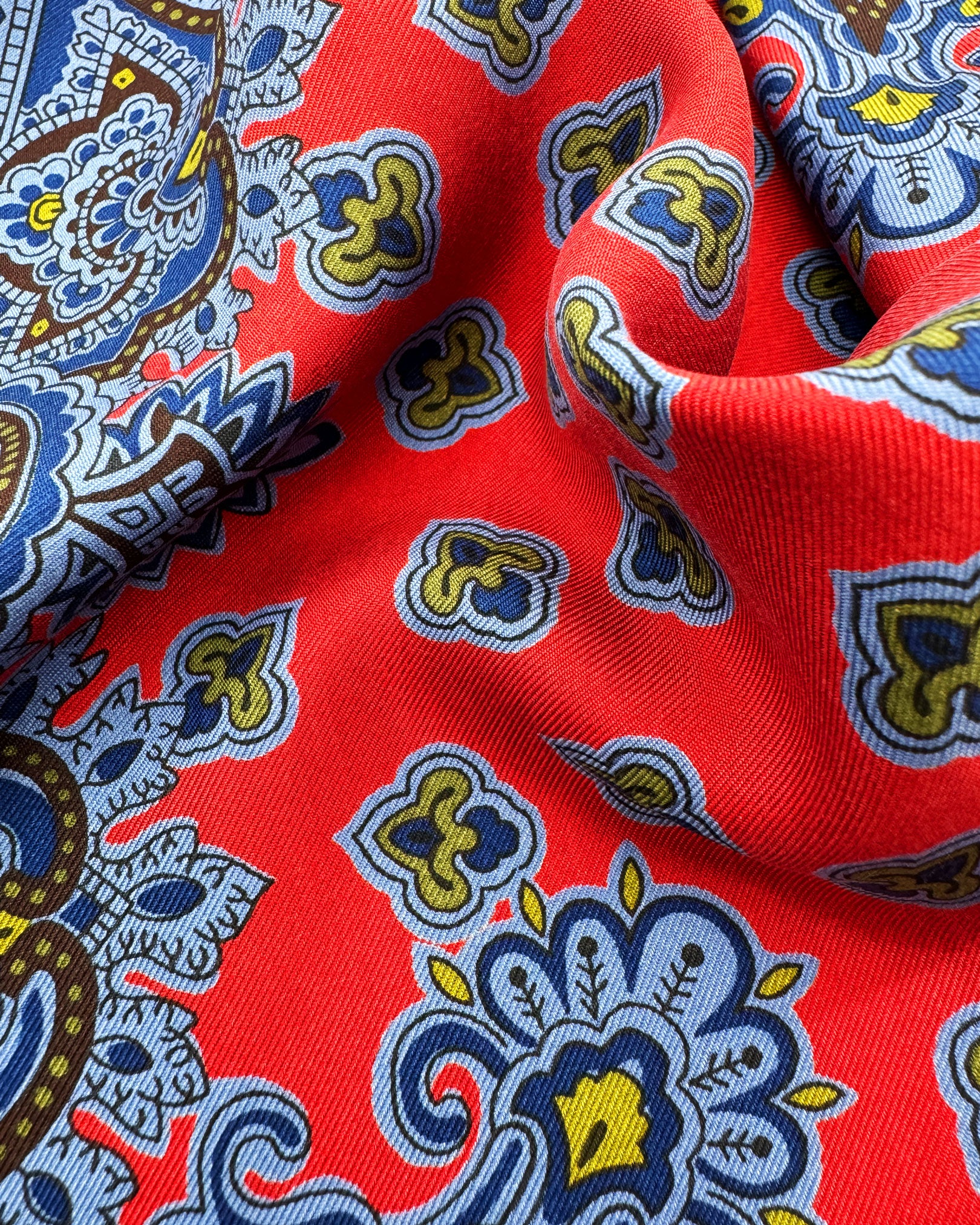 A ruffled close-up of the 'Aldborough' pocket square, presenting a closer view of the miniature fleur-de-lis patterns against the attractive lustre of the madder silk material. 