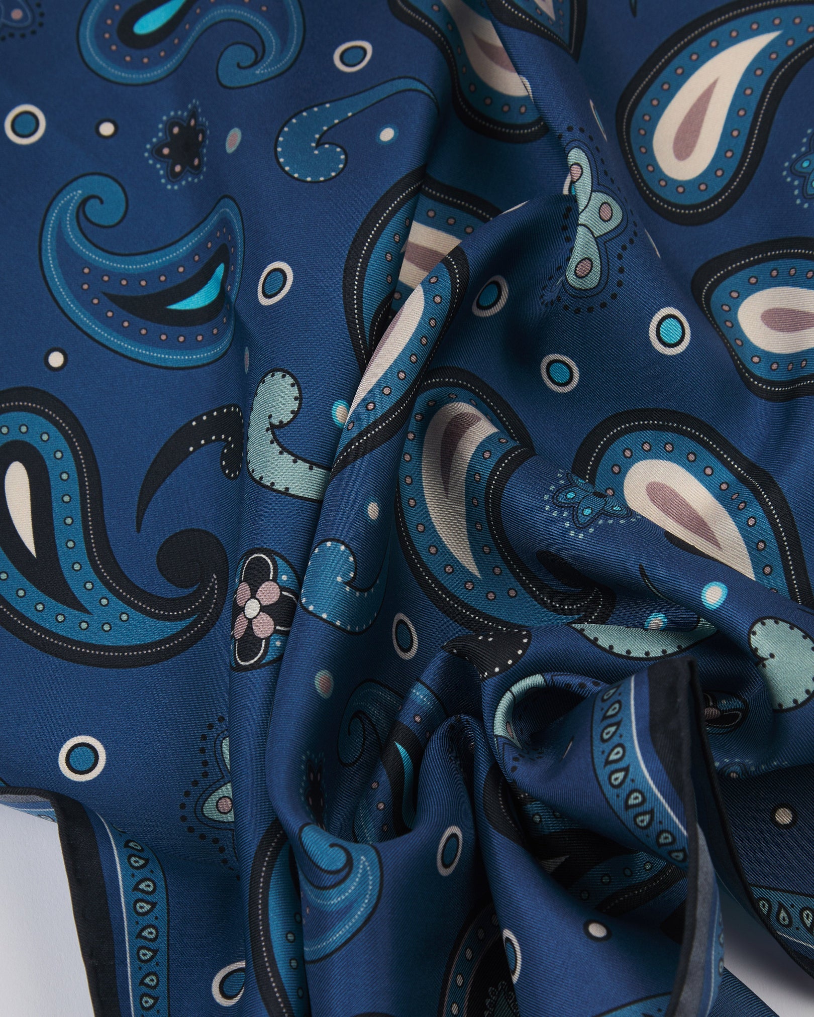 A ruffled close-up of the 'Belgravia' silk neckerchief from SOHO Scarves, revealing an elegant paisley-inspired pattern on a soft cornflower blue ground with a finely woven silk texture, accented by navy, sky blue and pale blush detailing.