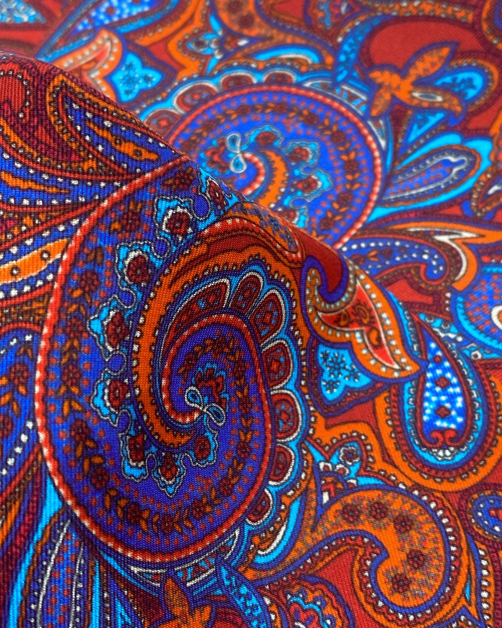 Ruffled close-up view of the Bretton silk scarf, presenting a closer view of the blue paisley patterns on a deep reddish-brown ground.