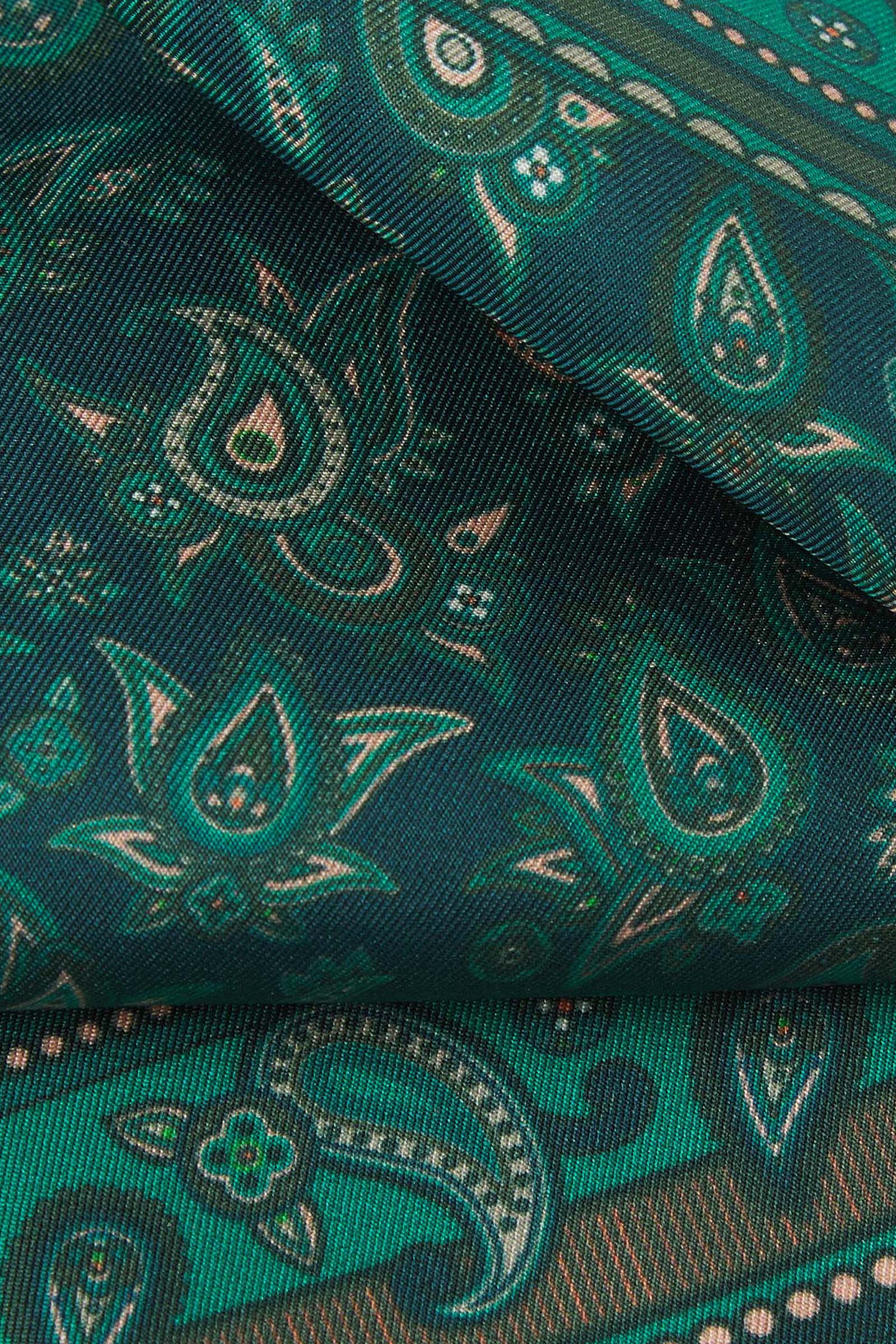 A ruffled close-up of the 'Buttermere' silk pocket square from SOHO Scarves, showing overlapping elements of the ornate border and paisley decoration against an emerald green background.