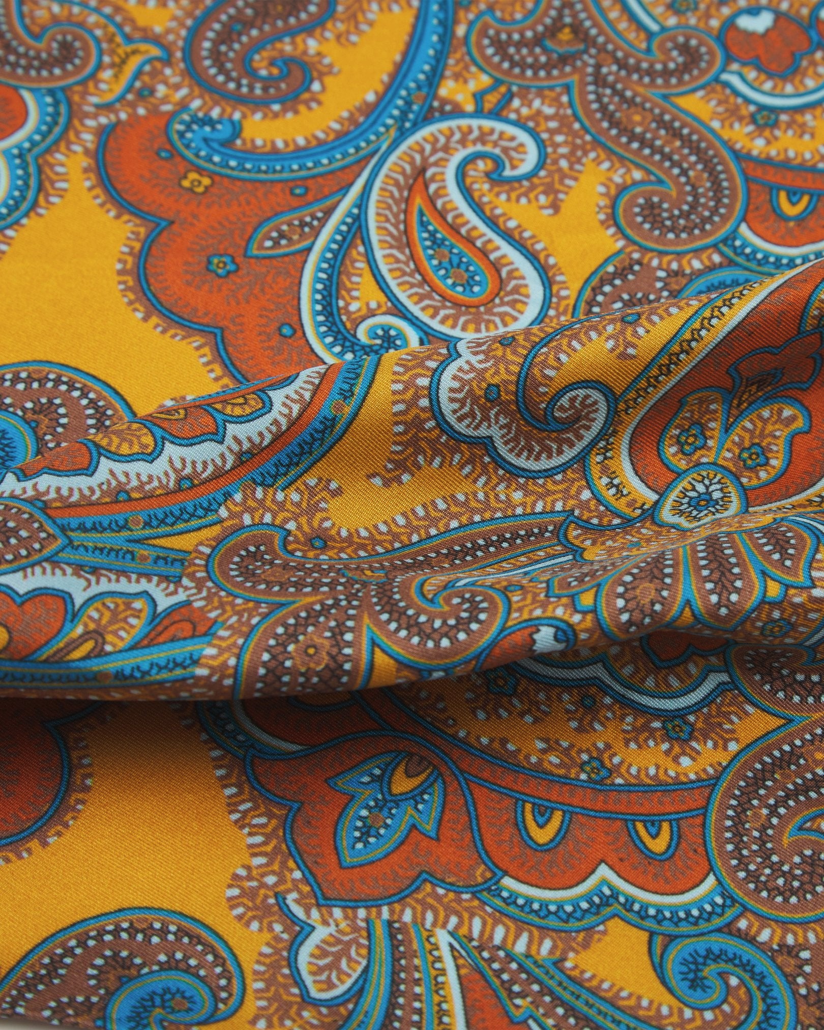 A ruffled close-up of the 'Carnaby' double ascot from SOHO Scarves, showing overlapping elements of the gold and cyan patterns against the lustre of the fine silk material.