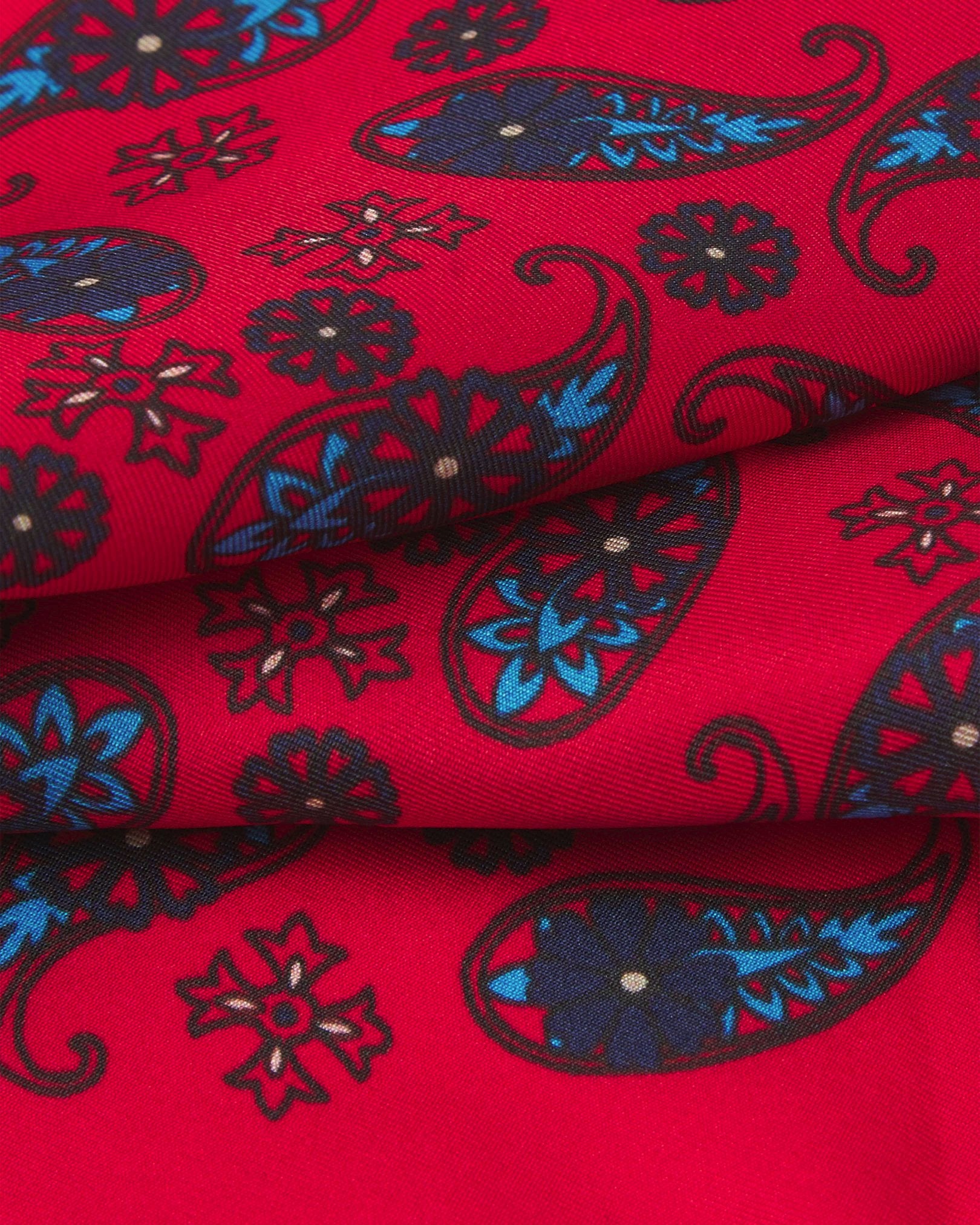 A ruffled close-up of the 'Casablanca' pocket square from SOHO Scarves, showing overlapping elements of simple blue paisley 'tears' interdispersed with decorative floral patterns against the lustre of the fine silk material.