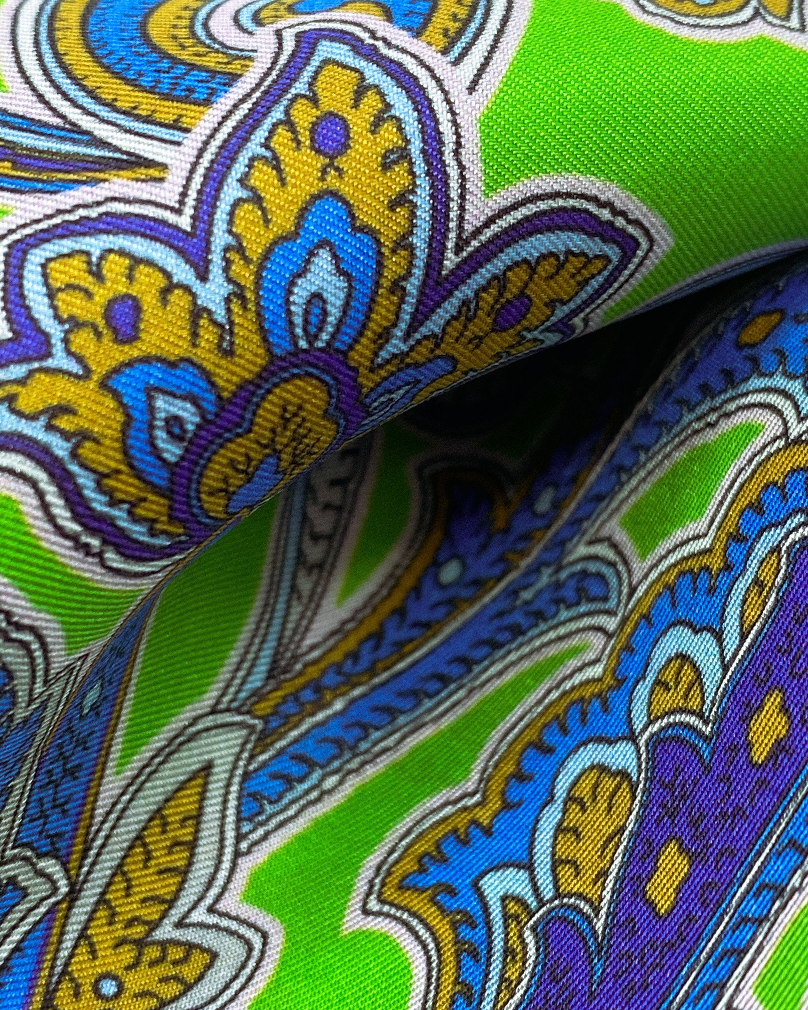 Ruffled close-up view of the 'Daytona' silk aviator scarf, presenting a closer view of the blue paisley swirls and floral symbols on a bright green background.