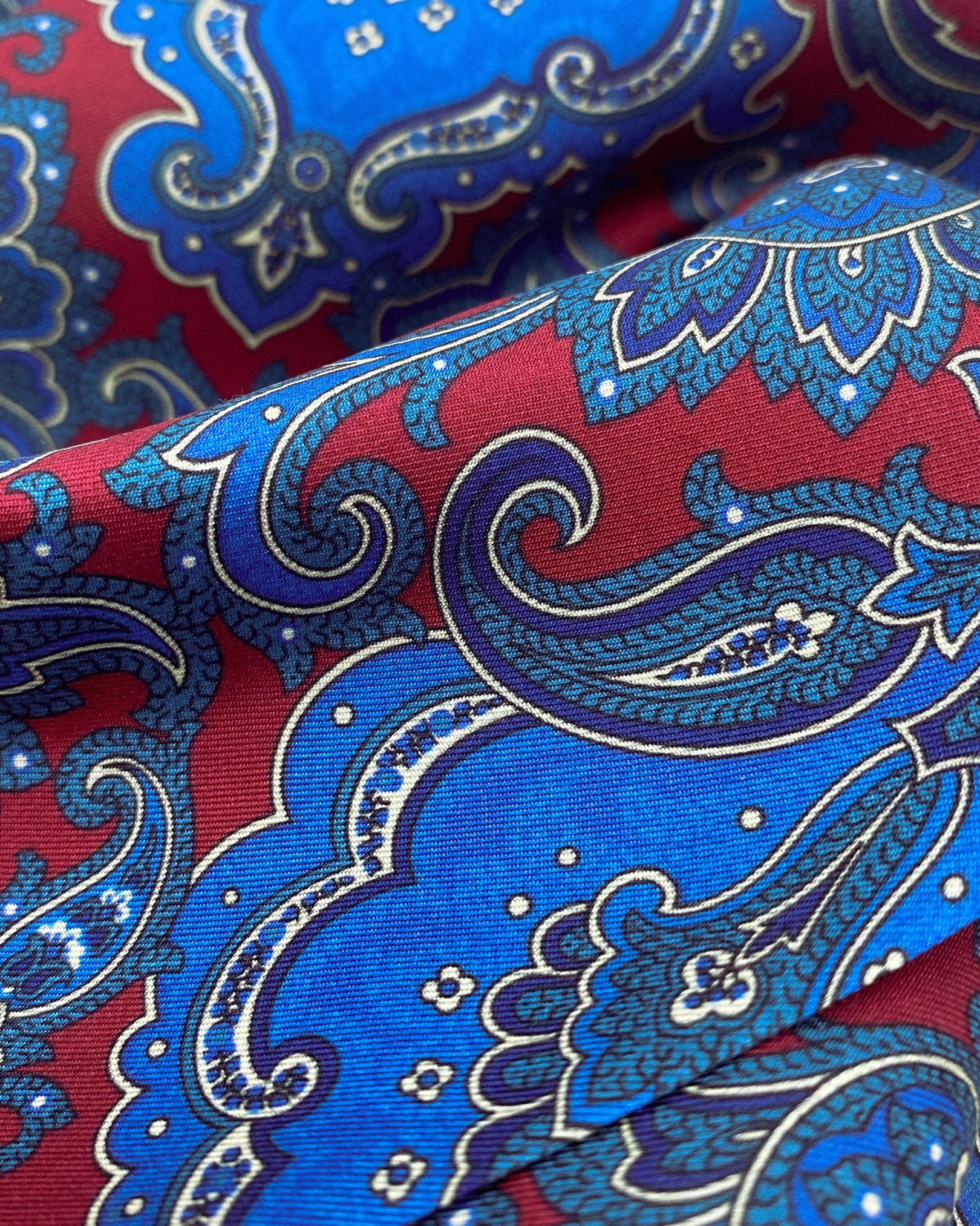 Ruffled close-up view of the 'Dean' silk scarf, presenting a closer view of the swirls of blue paisley intertwined with abstract floral patterns and subtle lustre of the material.