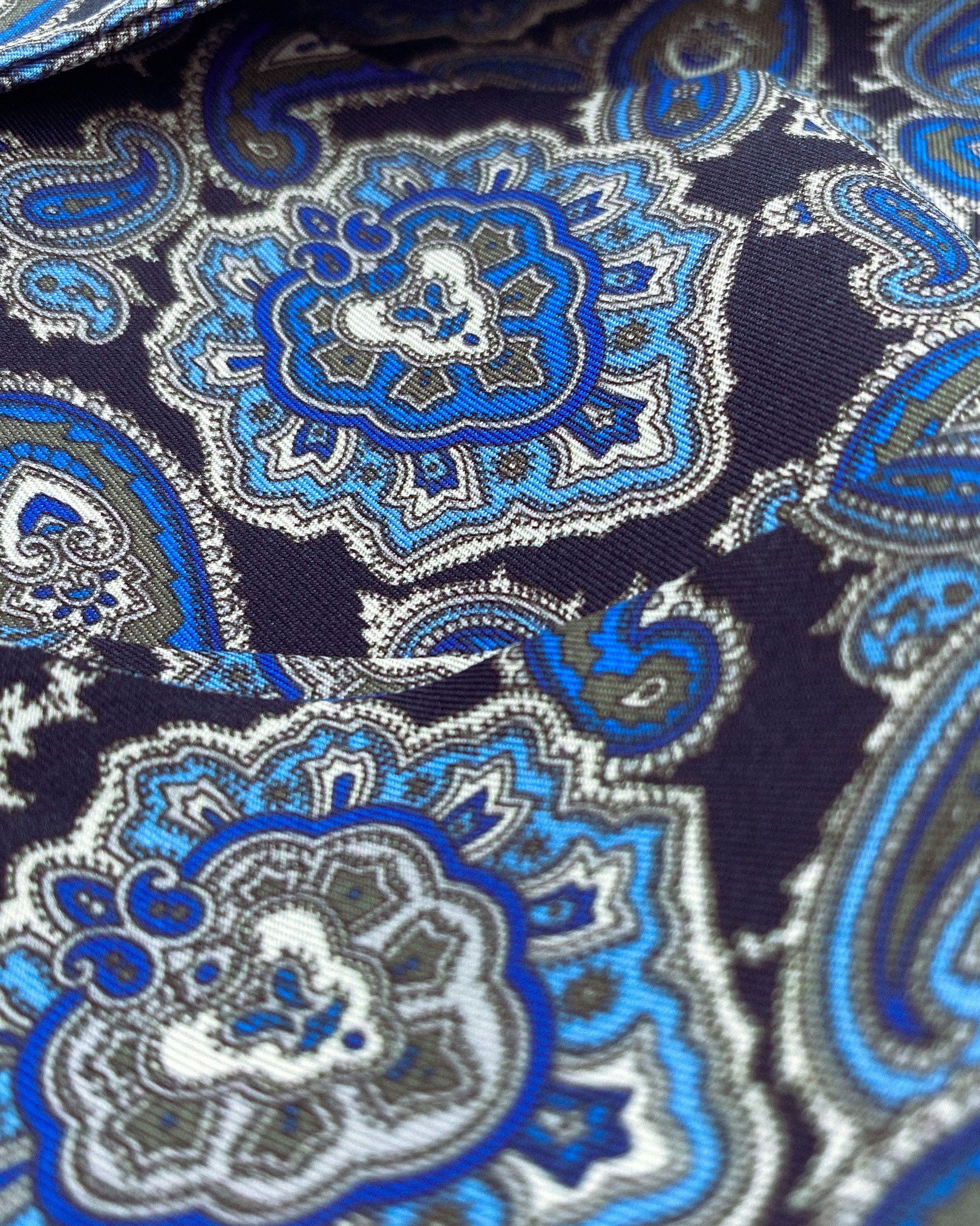 Ruffled close-up view of the Dezon silk aviator scarf, presenting a closer view of the blue paisley patterns on a dark blue background.