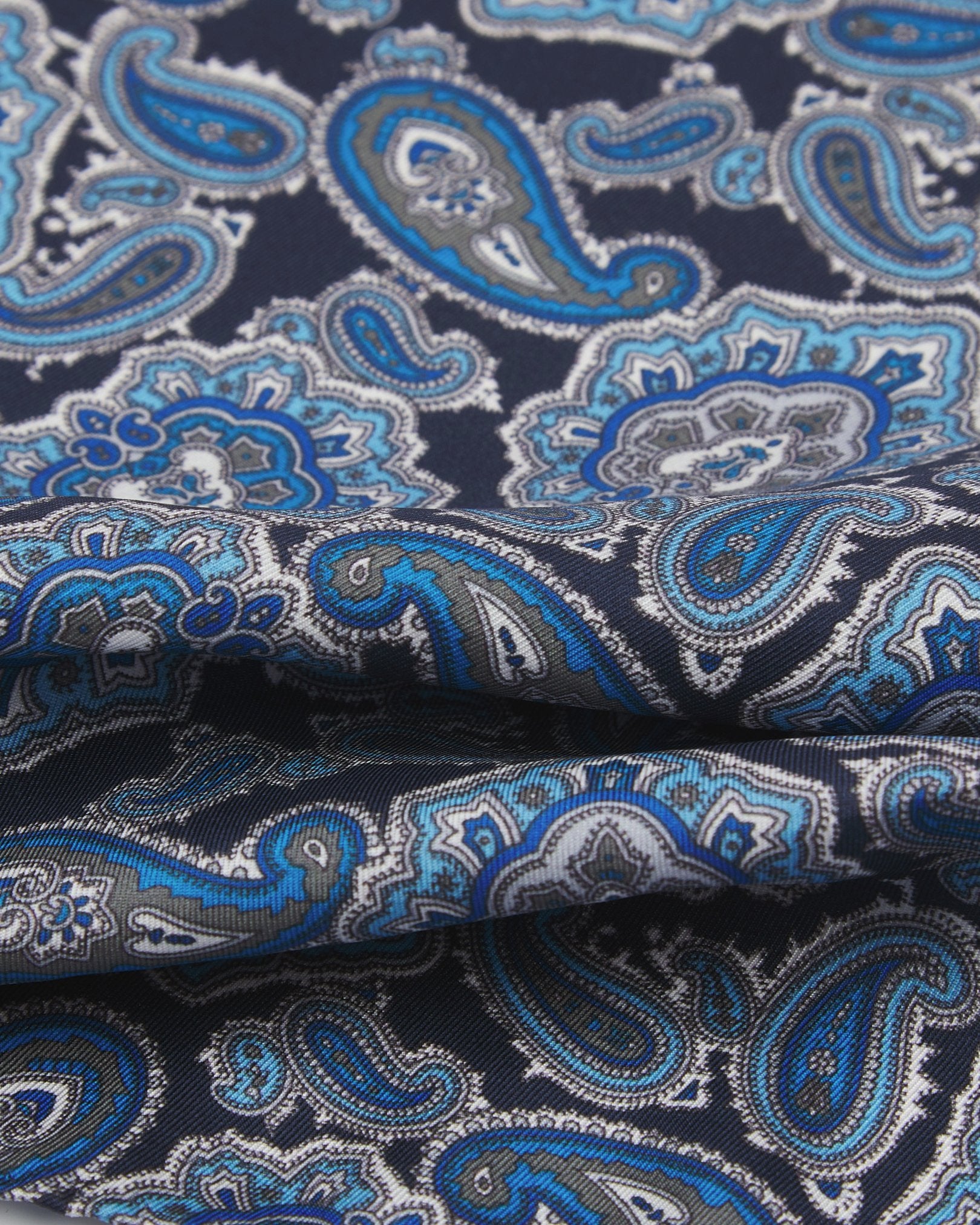 A ruffled close-up of the 'DeZon' silk pocket neckerchief from SOHO Scarves, showing overlapping elements of the blue paisley patterns.