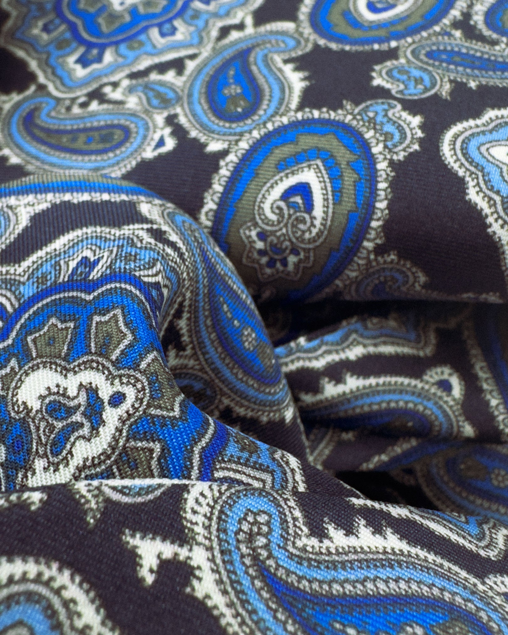 Ruffled close-up view of the Dezon silk scarf, presenting a closer view of the blue paisley patterns on a dark blue background.