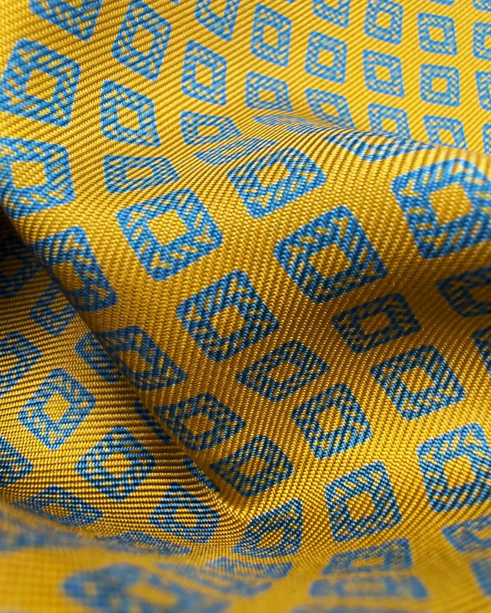 A ruffled close-up of the 'Dover' pocket square, presenting a closer view of hollow blue square patterns against the attractive lustre of the deadstock silk material. 