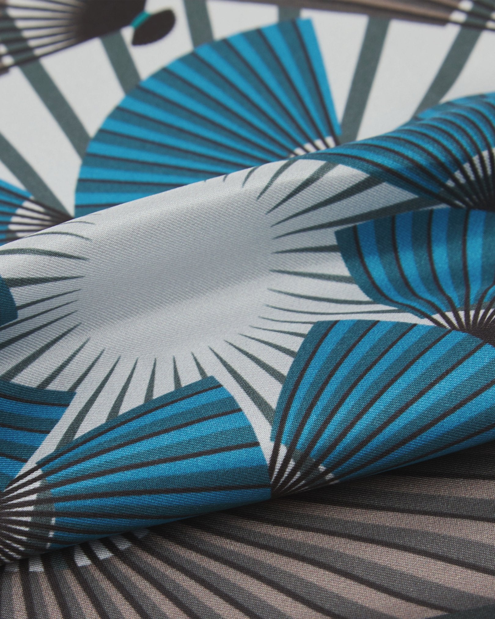 A ruffled close-up of the 'Fan' silk pocket square from SOHO Scarves, showing overlapping elements of the Japanese fan patterns in a cool, muted palette.