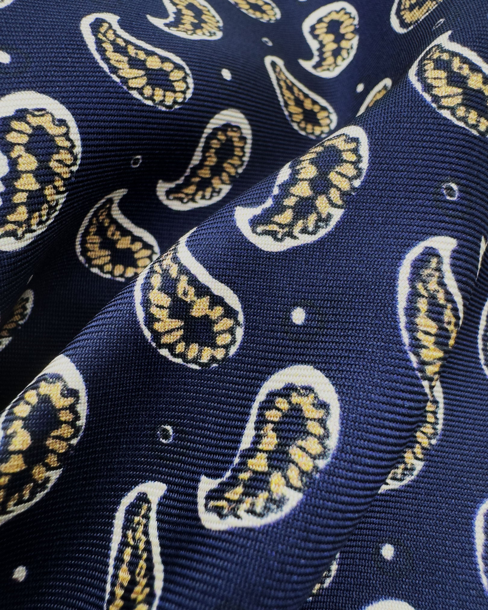 A ruffled close-up of the 'Hadrian' pocket square, presenting a closer view of the stylised paisley patterns in yellow and white against the attractive lustre of the deadstock silk material. 
