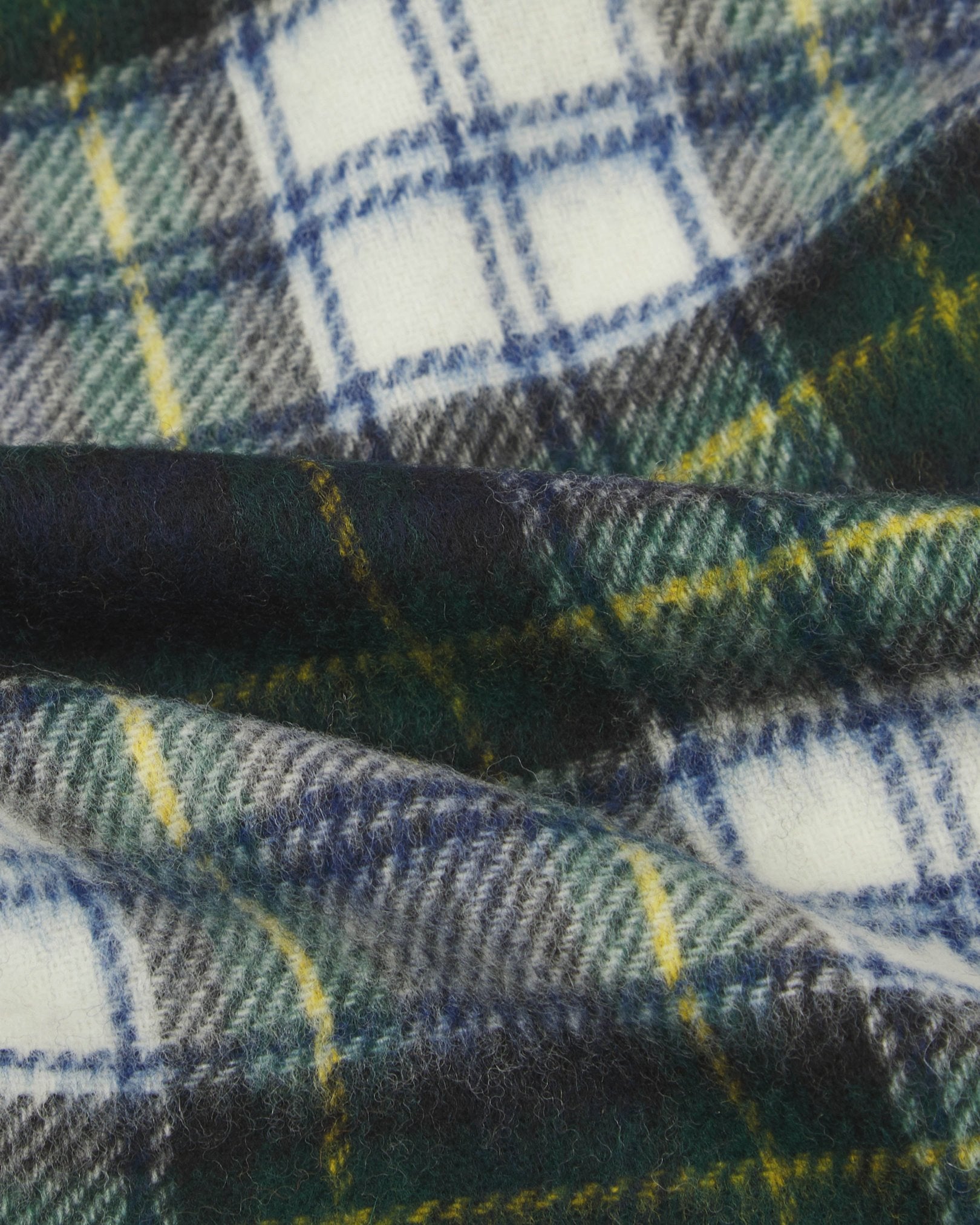 Ruffled close-up view of the UK-made, pure Merino wool 'Highlands' tartan in green scarf, presenting a closer view of the yellow, blue, cream and green interlocking tartan pattern.