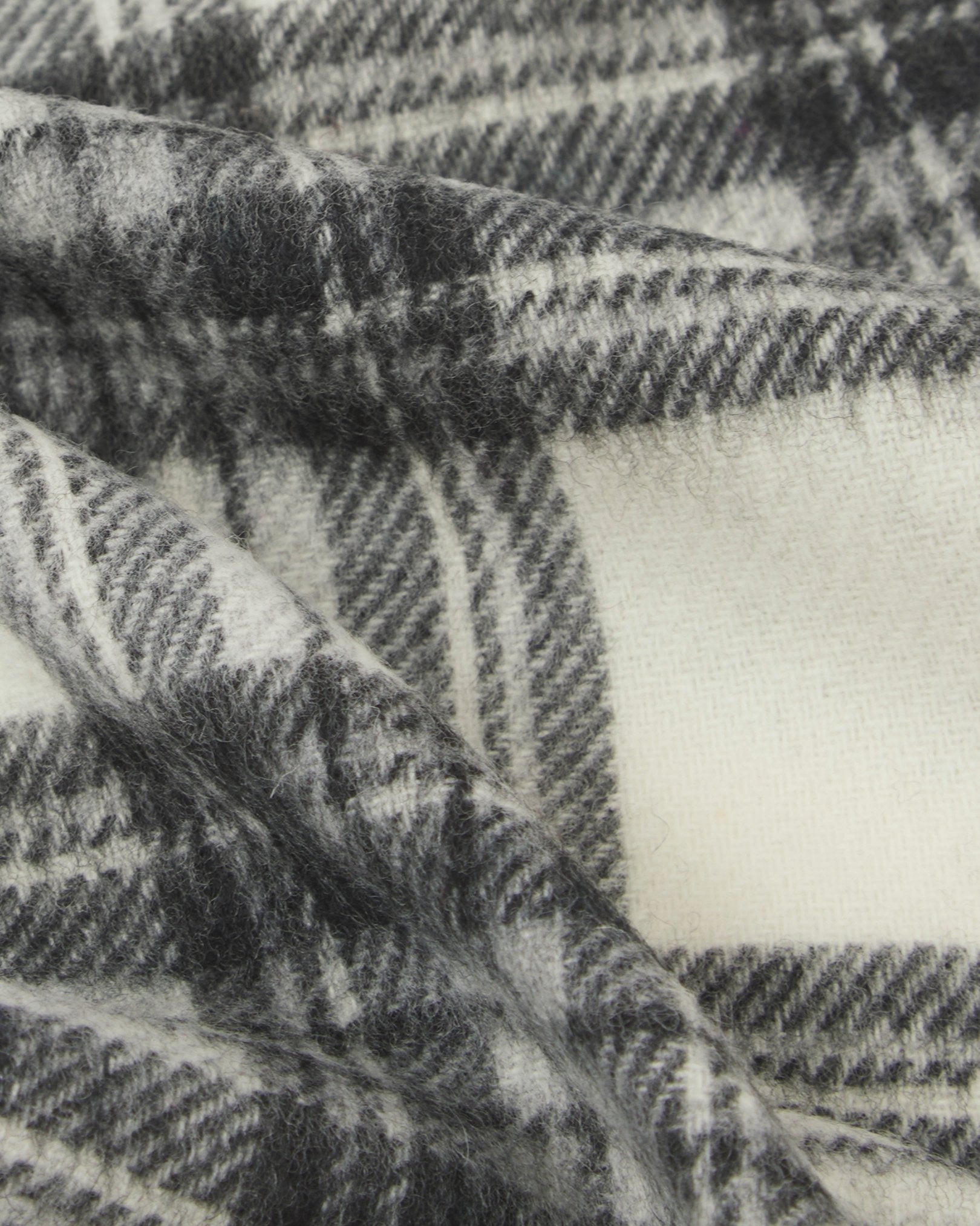 Ruffled close-up view of the UK-made, pure Merino wool 'Highlands' tartan in grey scarf, presenting a closer view of the grey, black and white interlocking tartan pattern.