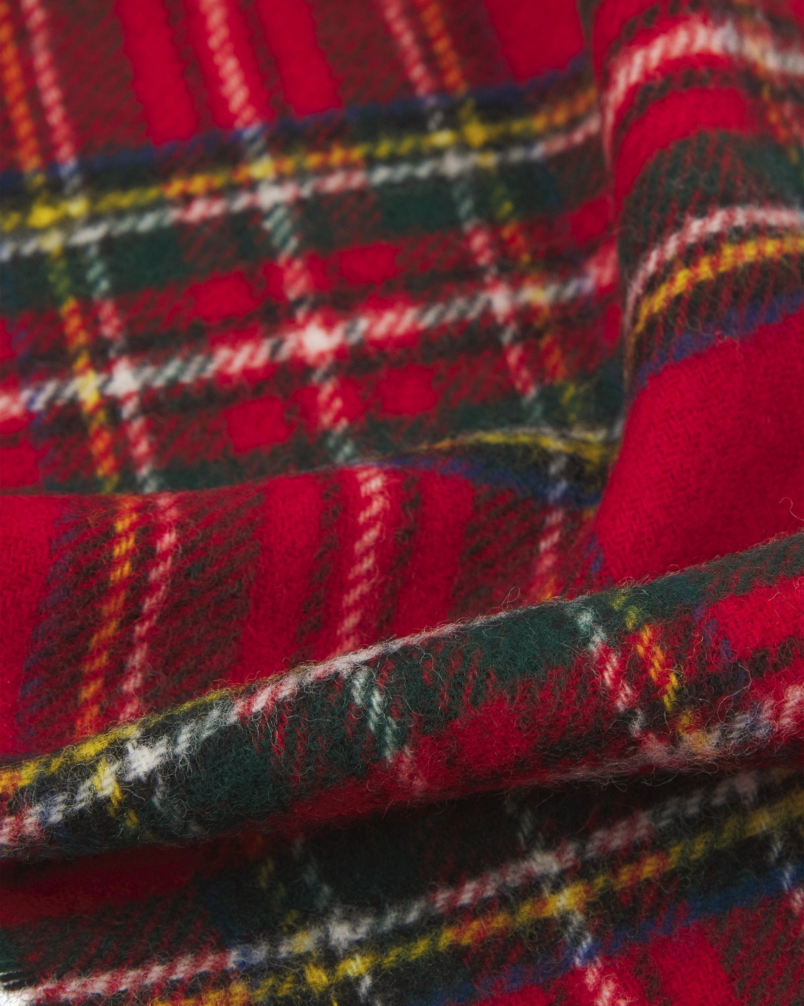 Ruffled close-up view of the UK-made, pure Merino wool 'Highlands' tartan in red scarf, presenting a closer view of the red, cream, blue, green, and yellow interlocking tartan pattern.