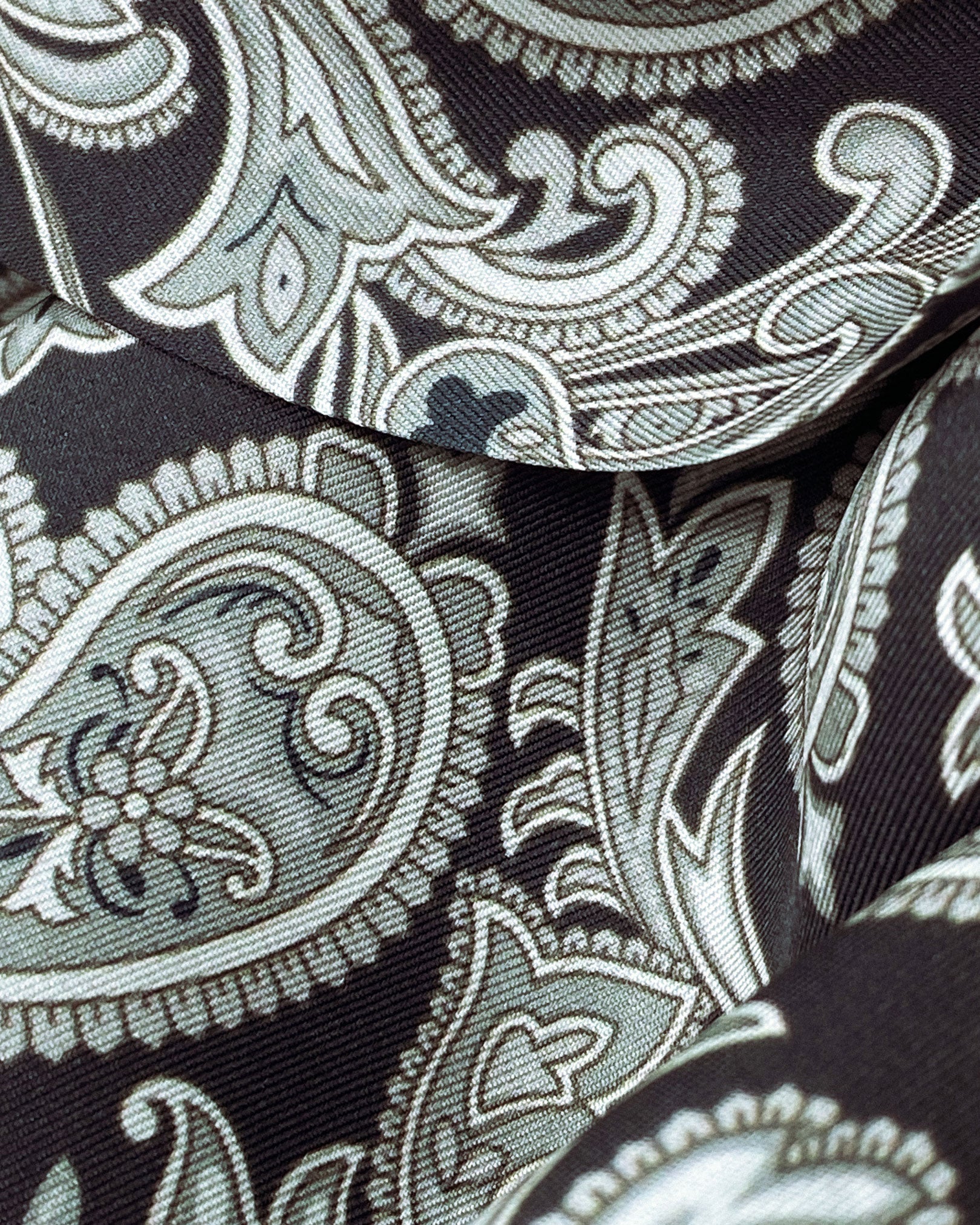 Ruffled close-up view of the Jaspar silk scarf, presenting a closer view of the monochrome paisley patterns.