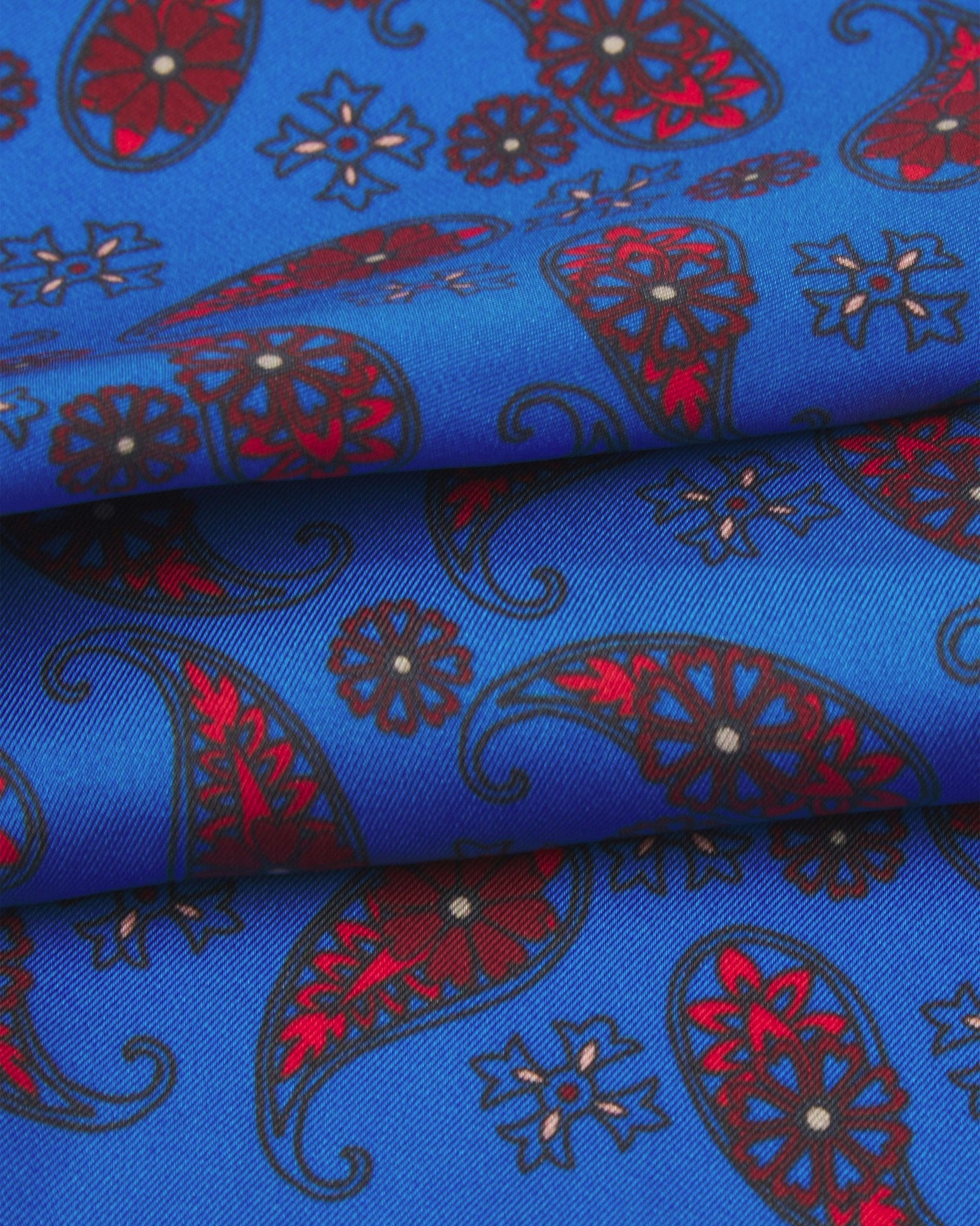 A ruffled close-up of the 'Marrakesh' pocket square from SOHO Scarves, showing overlapping elements of simple red paisley 'tears' interdispersed with decorative floral patterns against the lustre of the fine silk material.