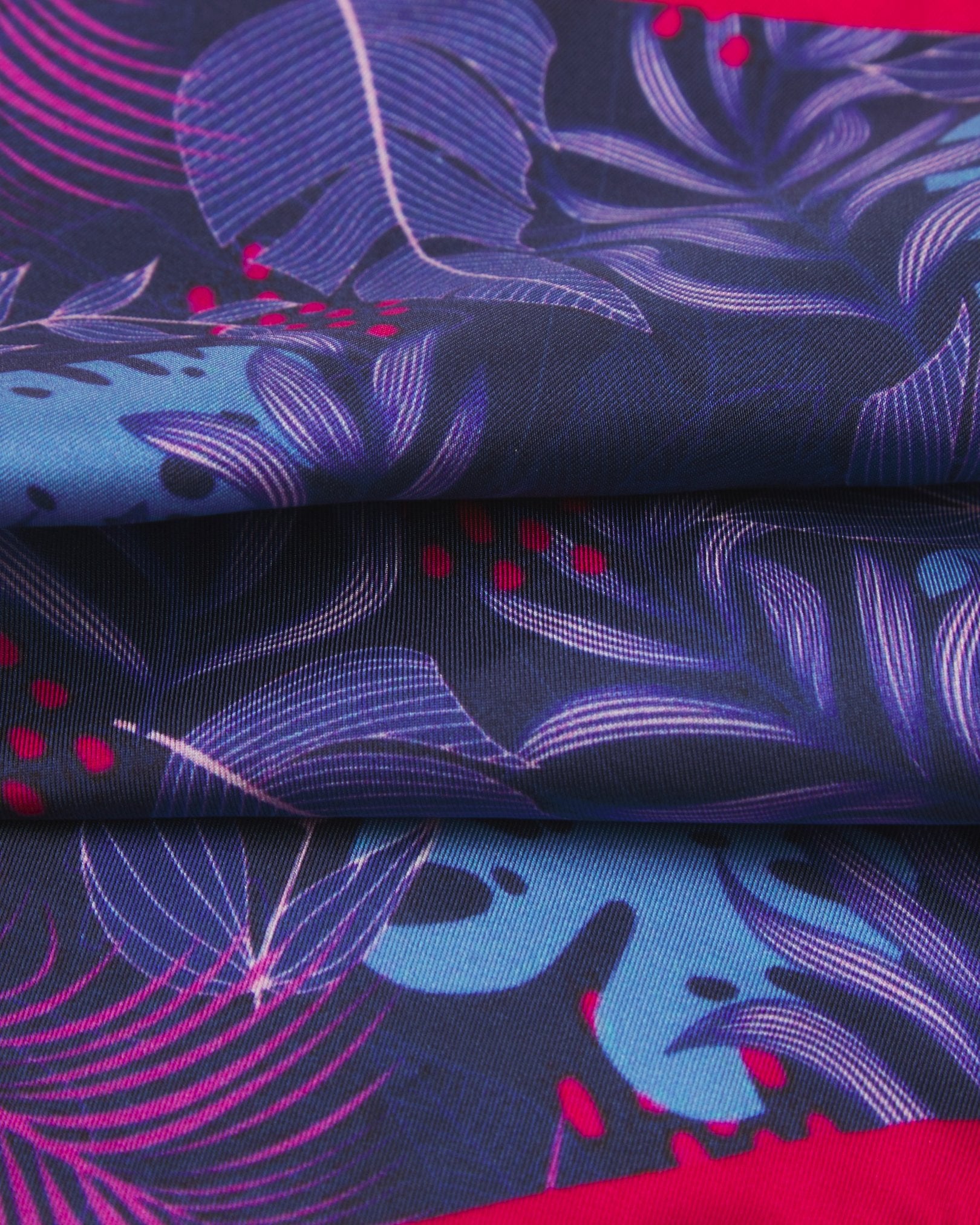 A ruffled close-up of the 'Mersey' silk pocket square from SOHO Scarves, showing the floral pattern on a purple-blue ground.