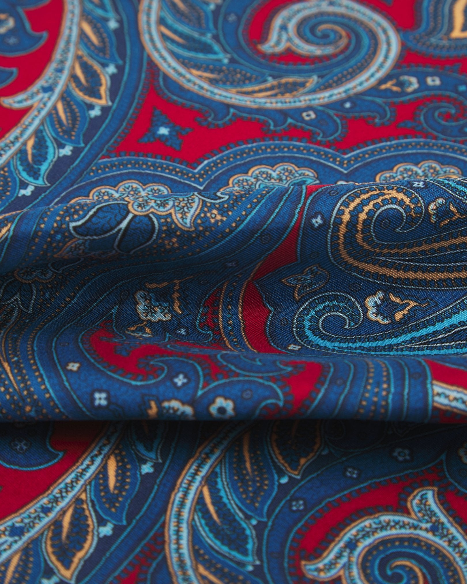 A ruffled close-up of the 'Oxford' double ascot from SOHO Scarves, showing overlapping elements of the showing the blue paisley patterns and surrounding floral patterns.