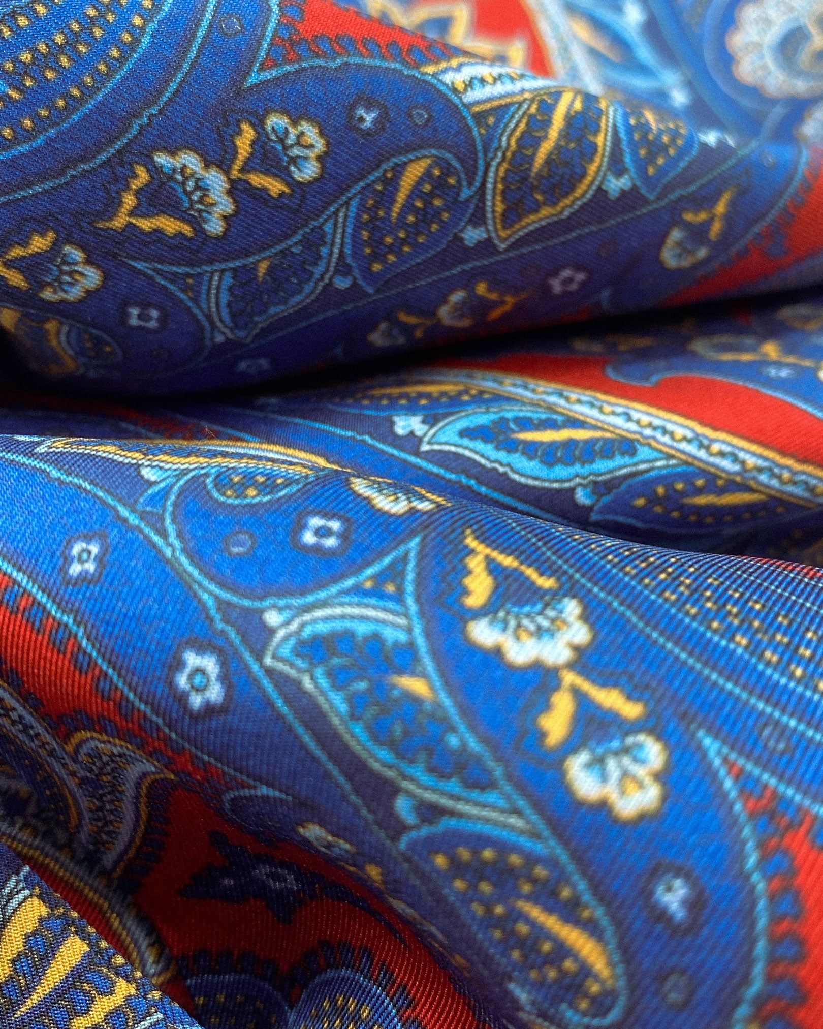 Ruffled close-up view of the Oxford silk aviator scarf, presenting a closer view of the intricate swirls of blue and red paisley and appealing lustre of the material.