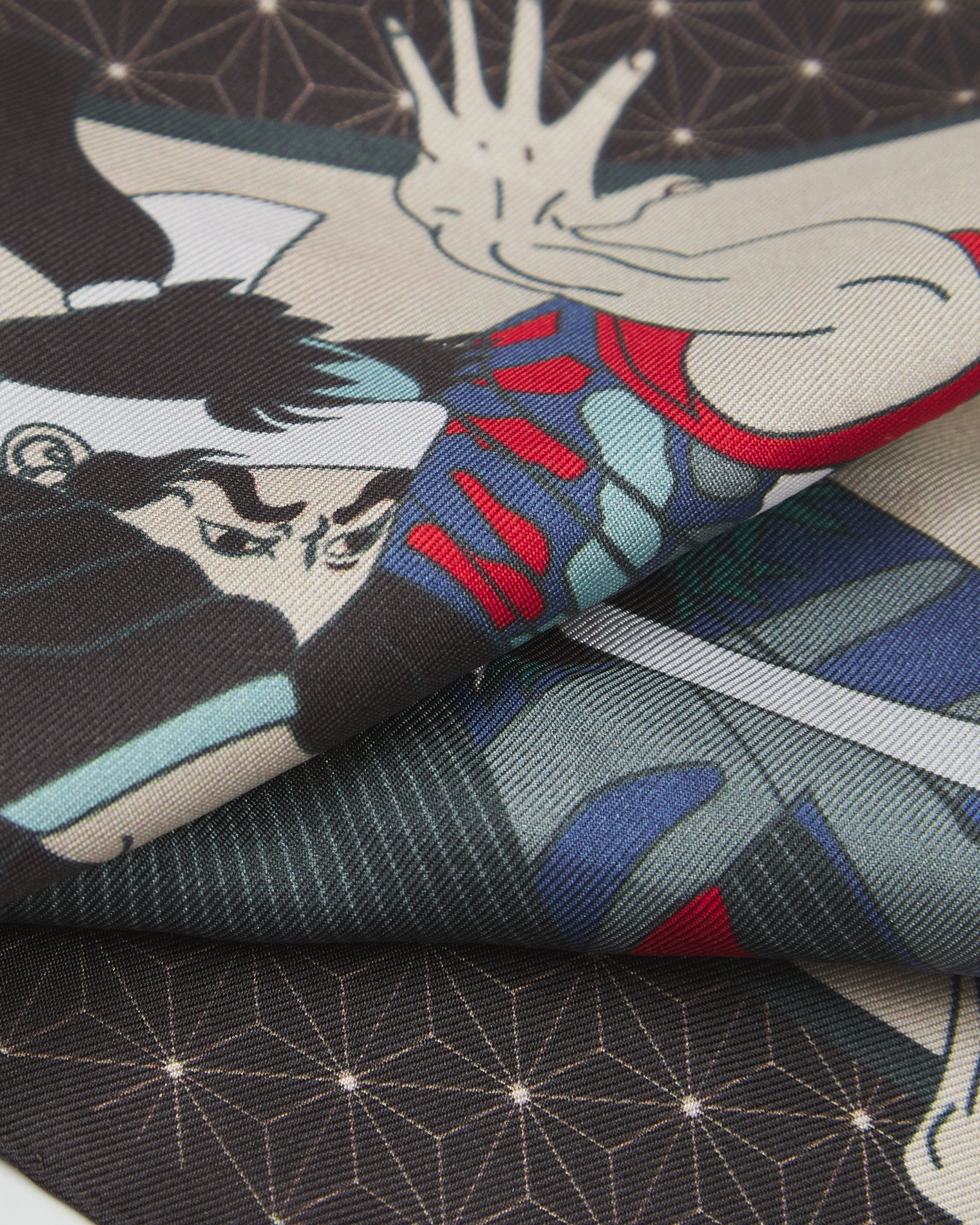 A ruffled close-up of the 'Samurai' silk pocket square from SOHO Scarves, showing overlapping elements of the Samurai and geometric patterned charcoal border.