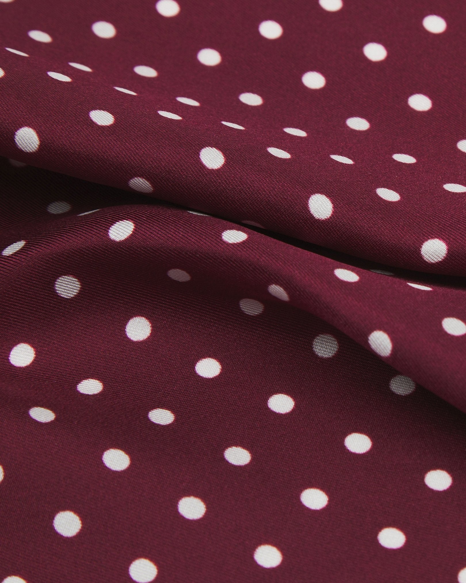 A ruffled close-up of the 'Sapporo' double ascot from SOHO Scarves, presenting a closer view of the burgundy fabric complemented by small white dots.