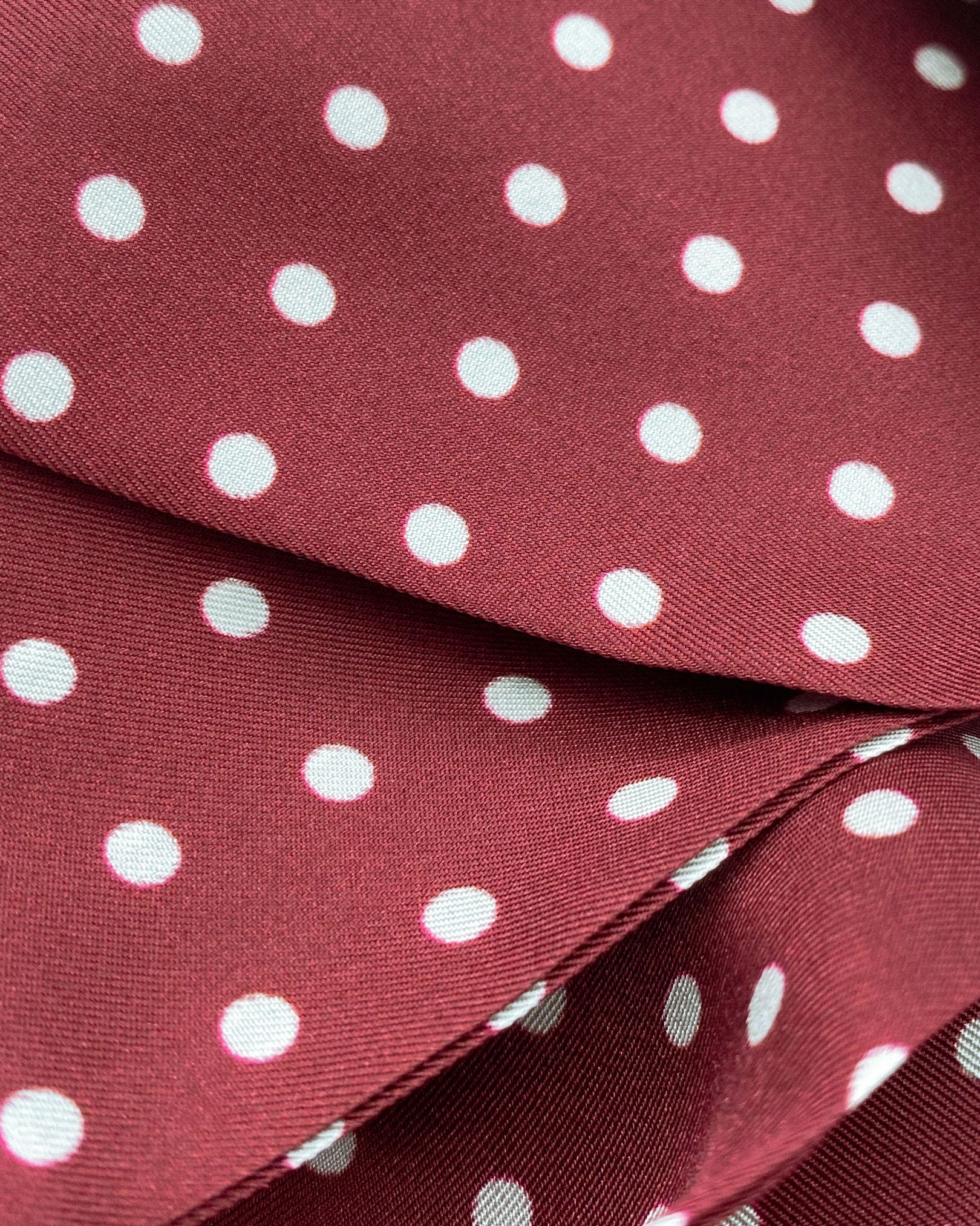 Ruffled close-up view of the Sapporo silk aviator scarf, presenting a closer view of the polka dot design in deep maroon with white dots and appealing lustre of the material.
