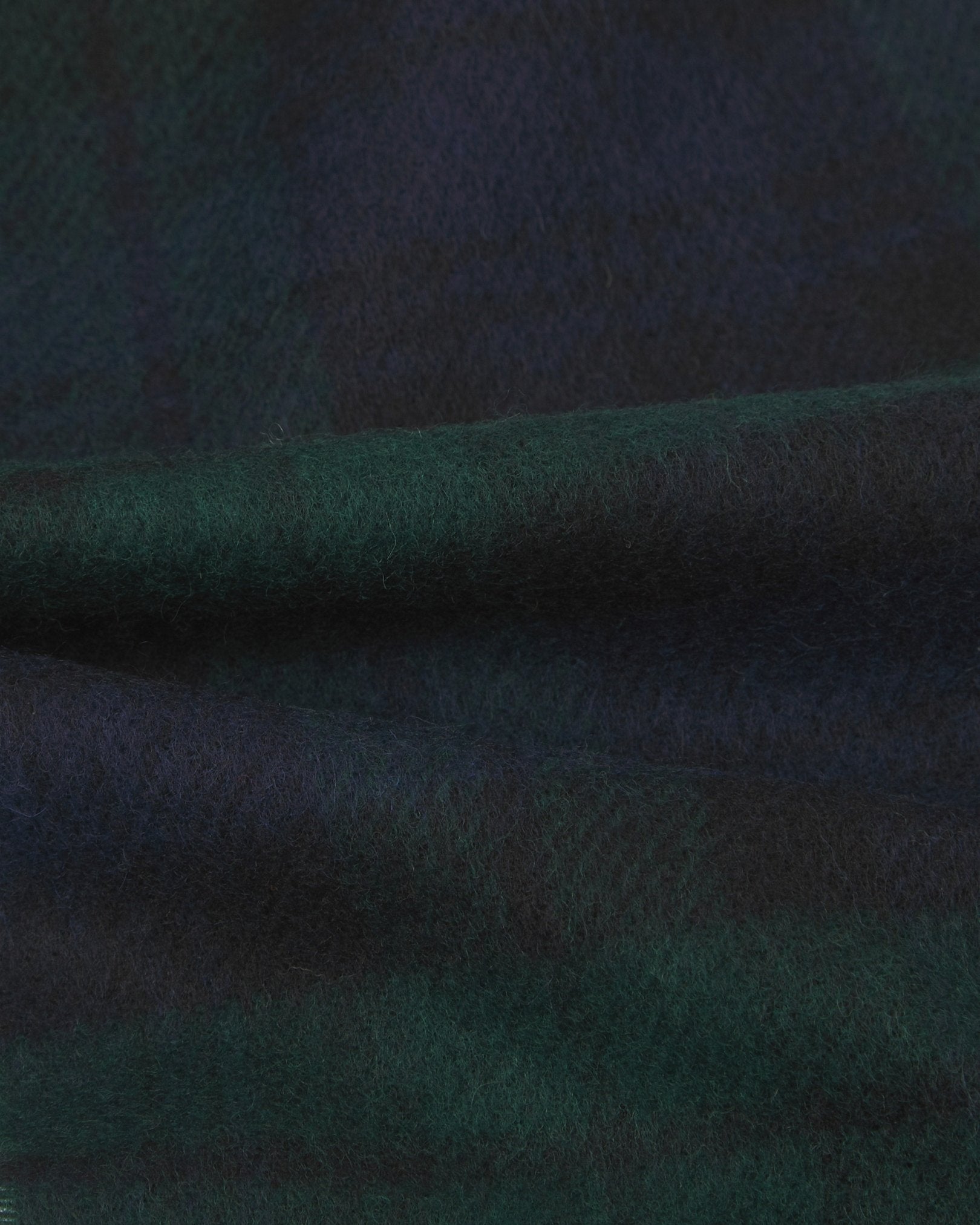 Ruffled close-up view of the UK-made, pure Merino wool 'Shetland' tartan in green scarf, presenting a closer view of the navy, green and black interlocking tartan pattern.